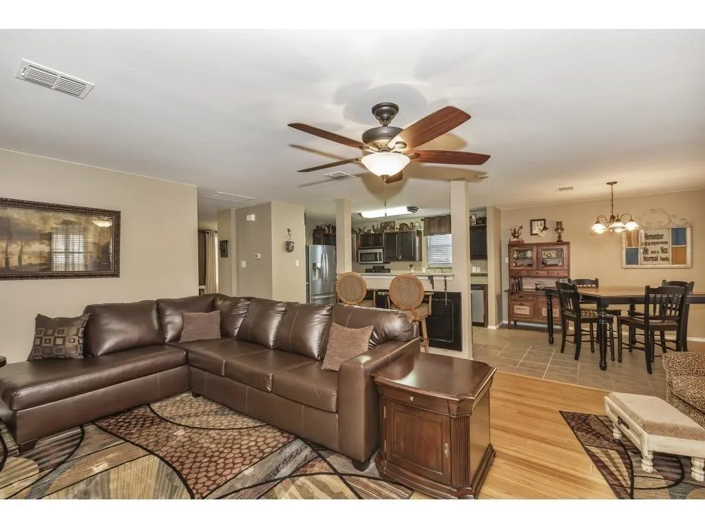 Spacious living area featuring wood-finish flooring, a ceiling fan with integrated lighting, and neutral wall​​‌​​​​‌​​‌‌​‌‌​​​‌‌​‌​‌​‌​​​‌​​ tones