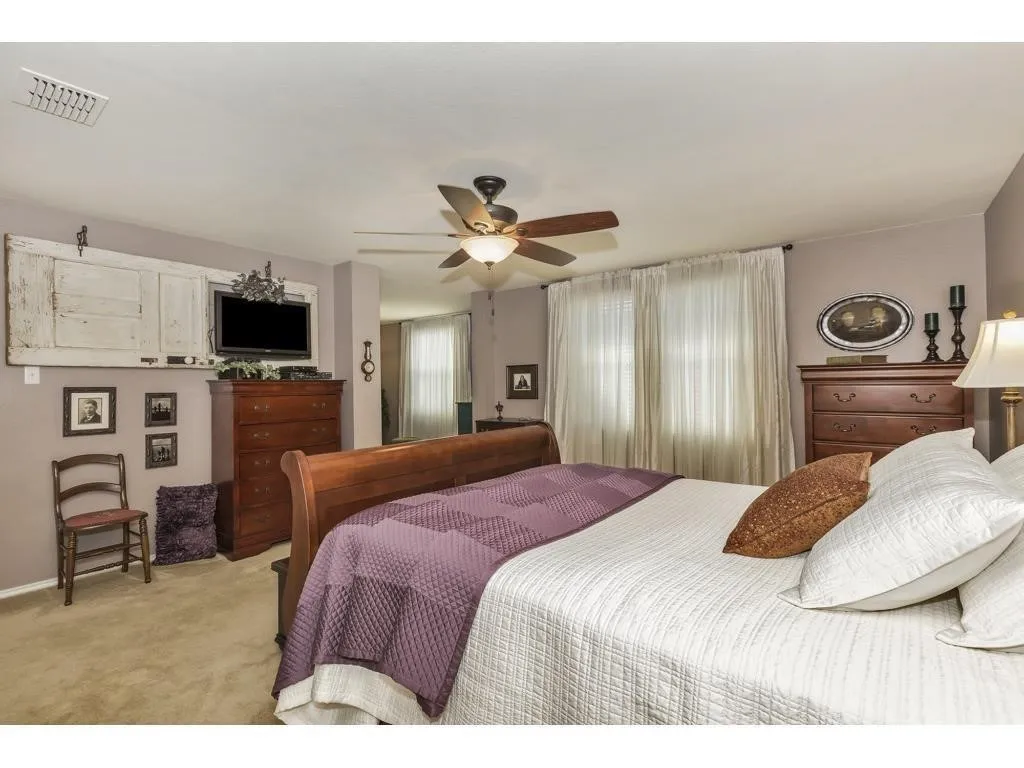 Carpeted bedroom featuring a ceiling fan with integrated lighting, window with sheer curtains, and a built-in wall niche