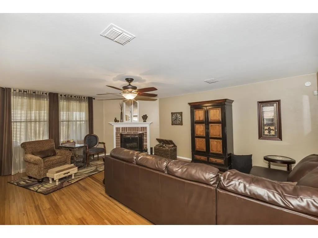 Living area featuring wood-finish flooring, a brick fireplace with a white mantel, and multiple windows with blinds
