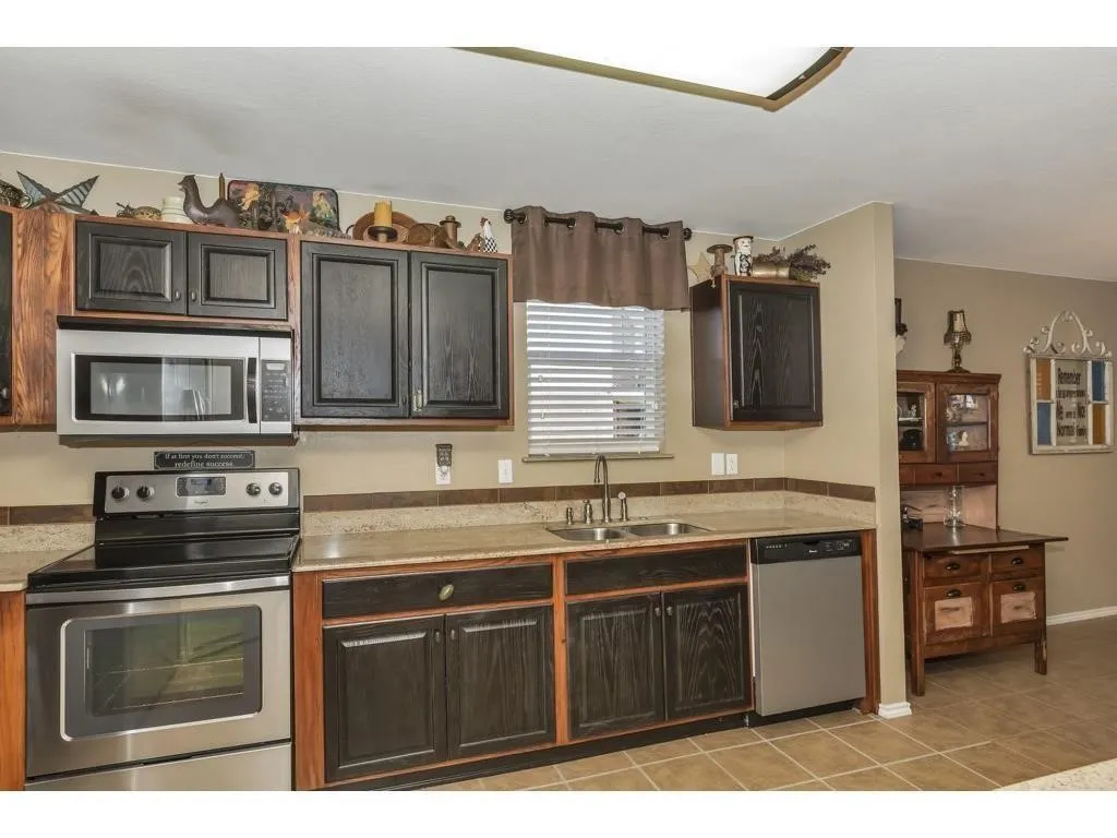 Kitchen featuring wood-finish cabinetry, stainless steel appliances, a double basin sink, light-toned countertops, and tile flooring