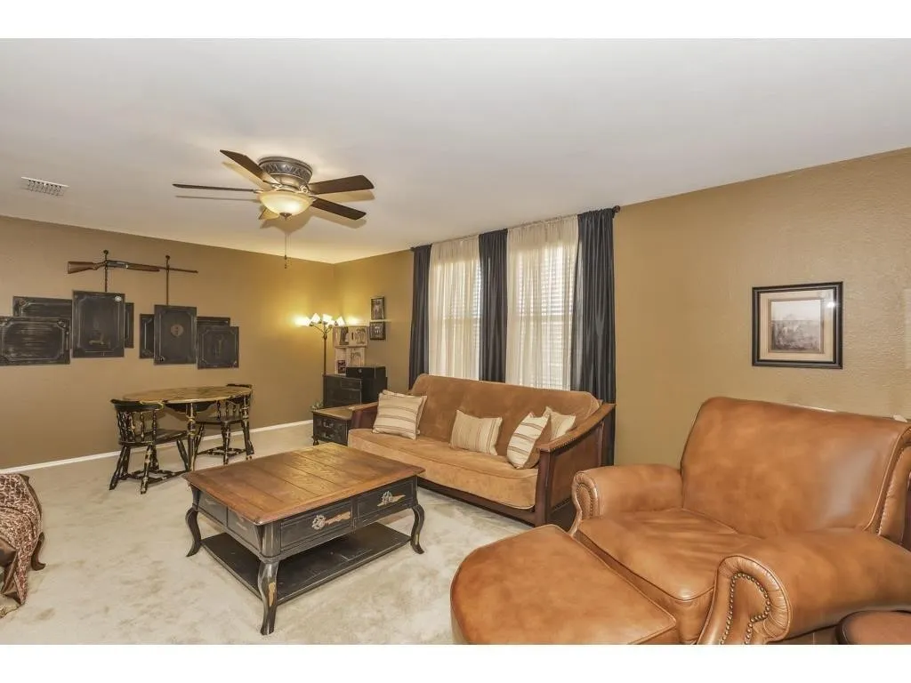 Carpeted living area featuring a ceiling fan with integrated lighting, textured walls, and windows with blinds and drapery