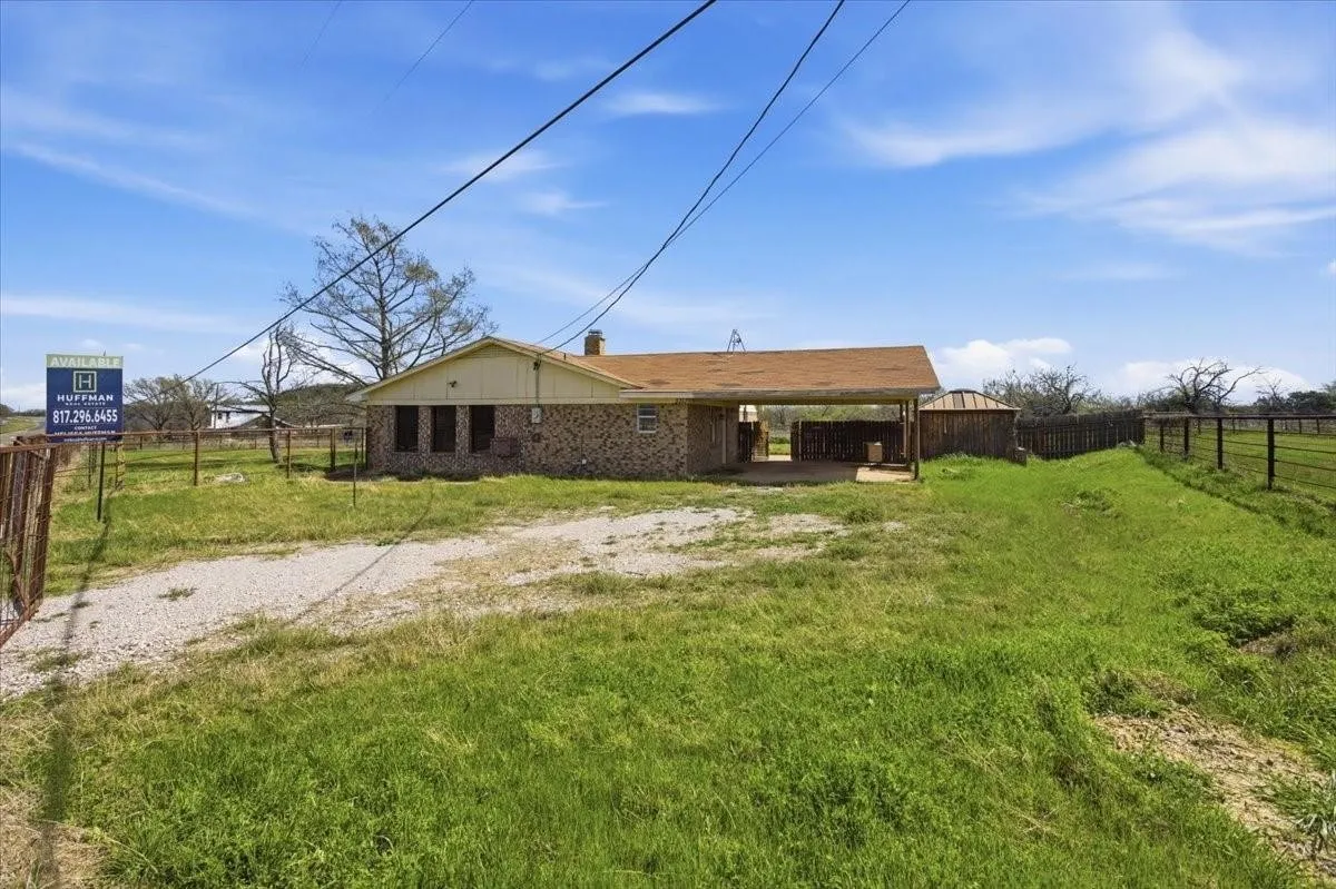 Single-story residence featuring a brick facade, covered carport, and a gravel driveway