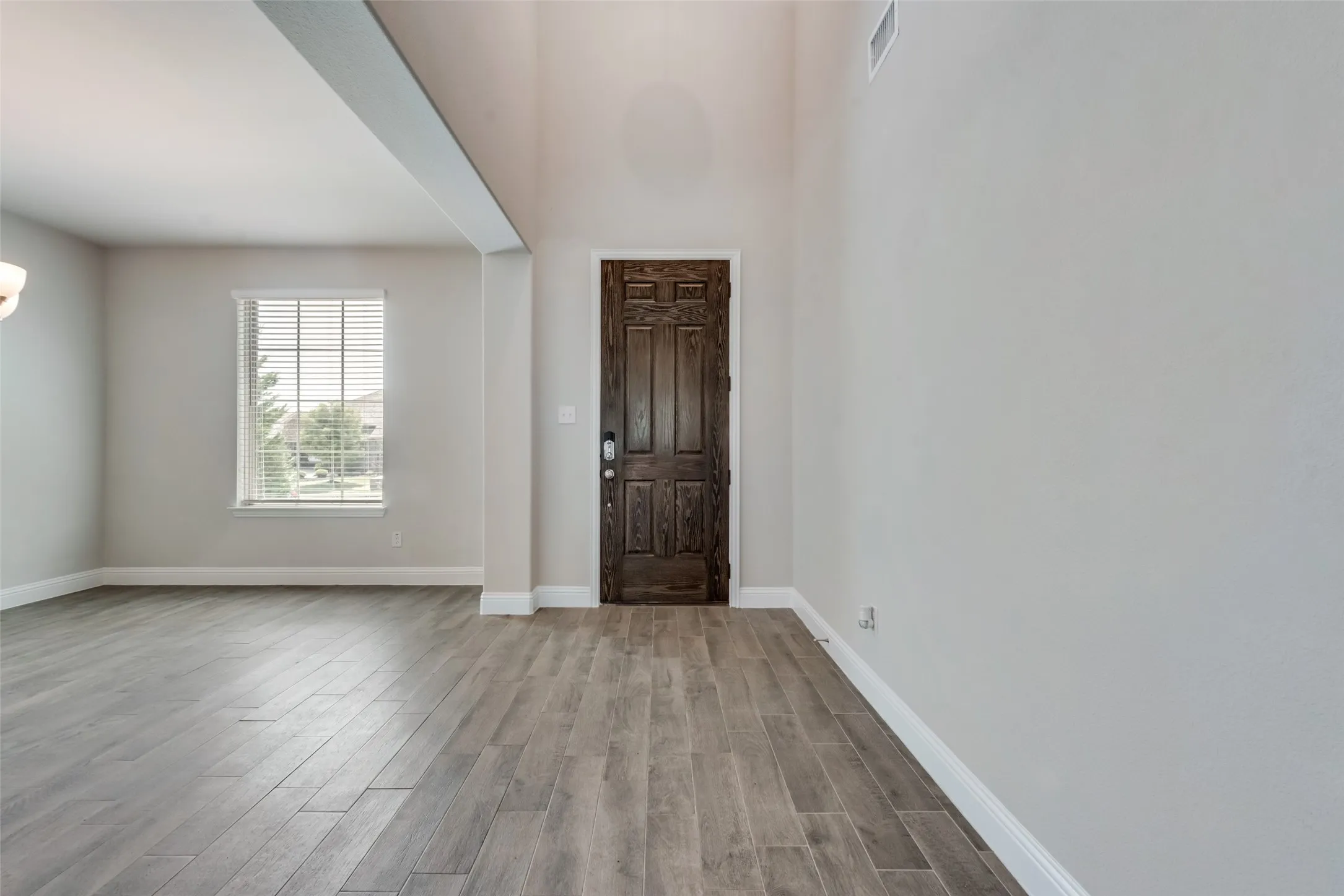 Entryway featuring a dark wood door with decorative panels, wood-finish tile flooring, and high ceilings