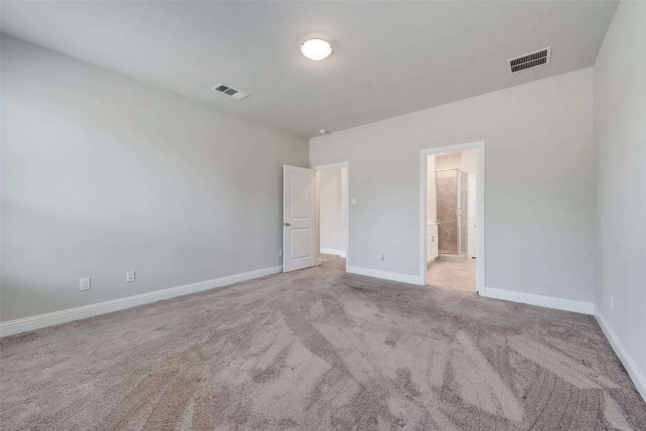 Spacious room featuring light gray walls, plush gray carpeting, and white baseboards