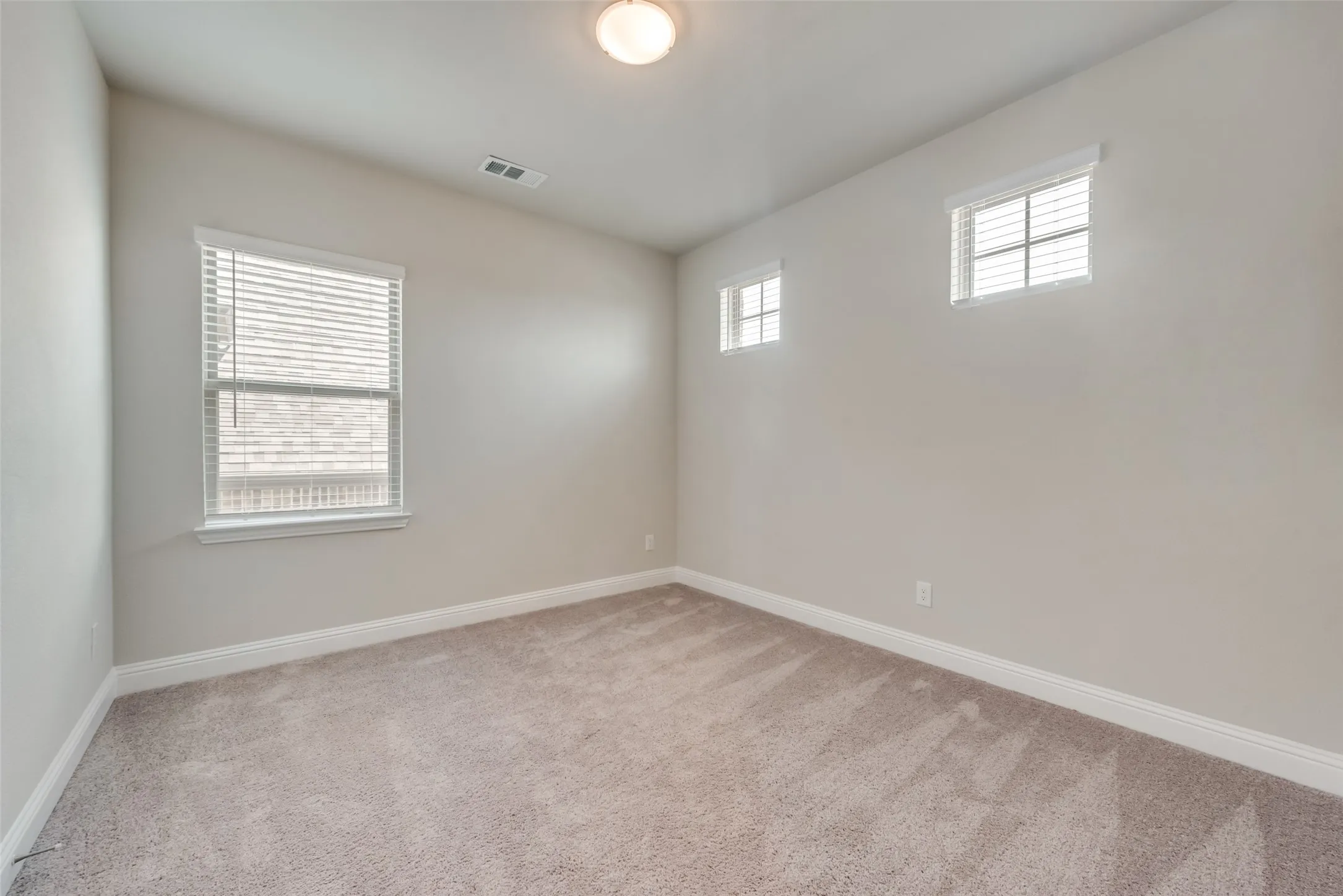 Neutral-toned carpeted room featuring a large window with blinds, two smaller horizontal windows with blinds, a flush mount ceiling light, and baseboard molding