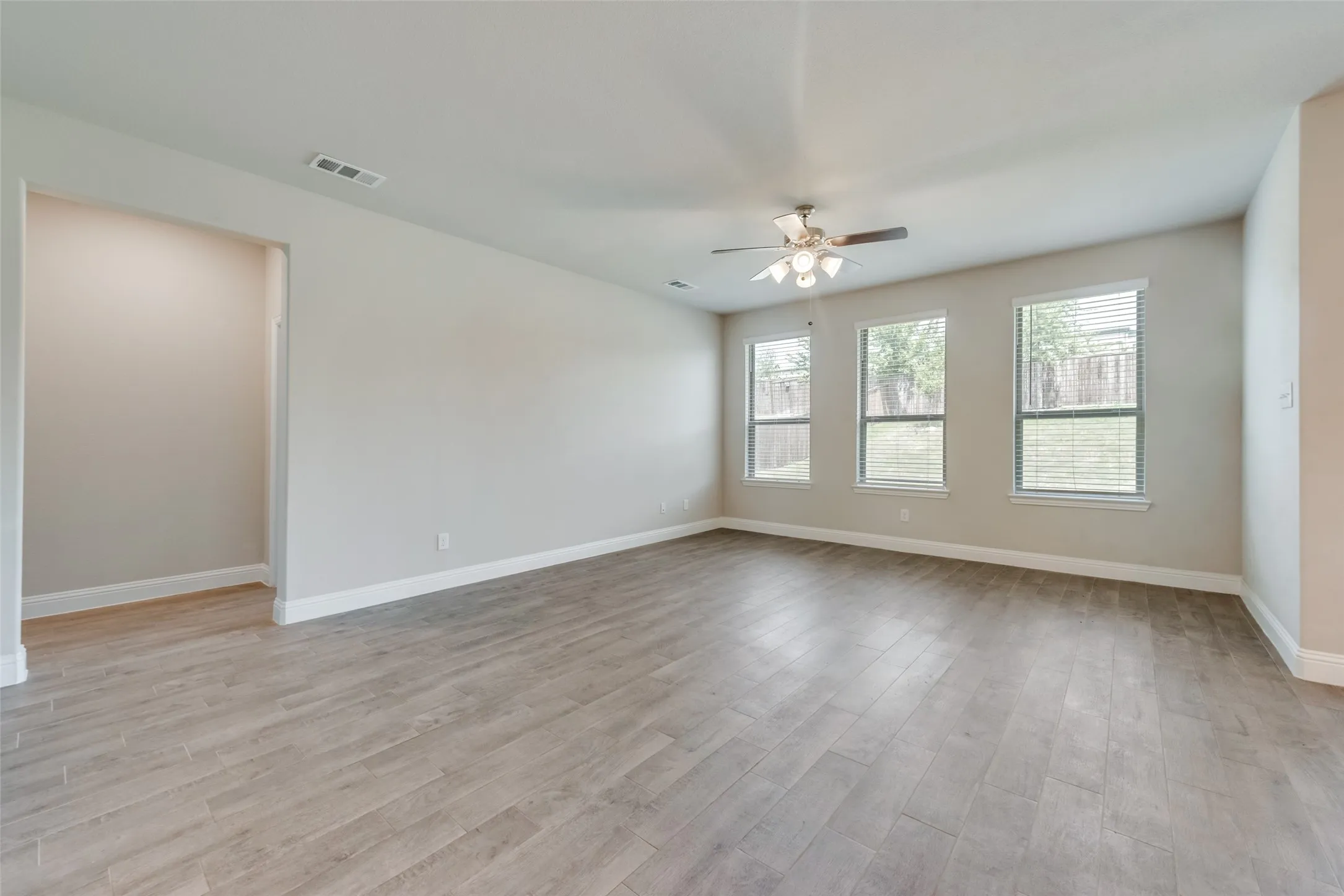Spacious room featuring wood-finish flooring, light neutral wall tones, and white baseboards