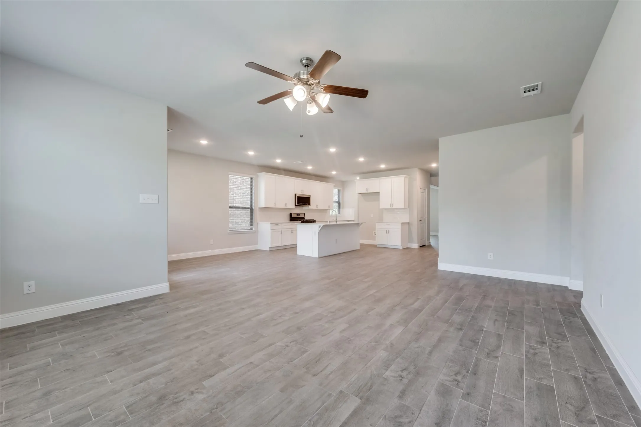 Spacious living area featuring plank-style wood-finish flooring, a ceiling fan with integrated lighting, and recessed ceiling lights
