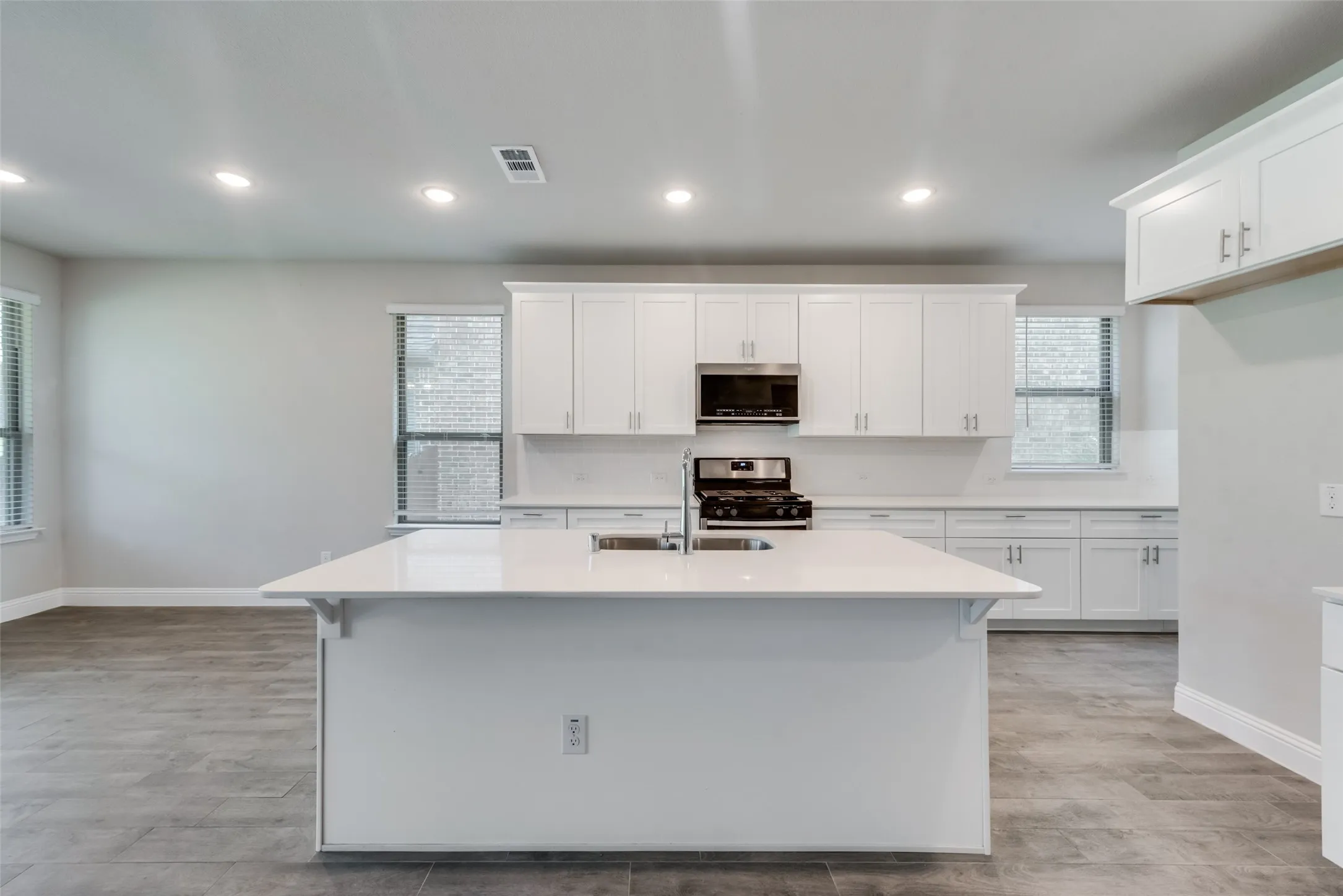 Spacious kitchen featuring an island with an integrated sink, white cabinetry, stainless steel appliances, and light-toned countertops