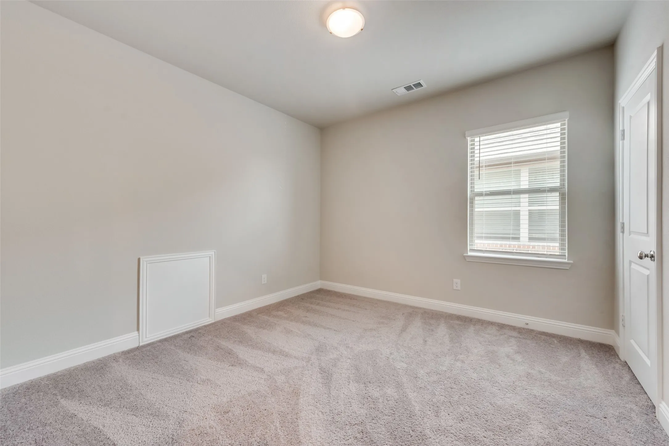 Spacious room featuring neutral wall paint, light-colored carpet flooring, a single window with blinds, and a white interior door
