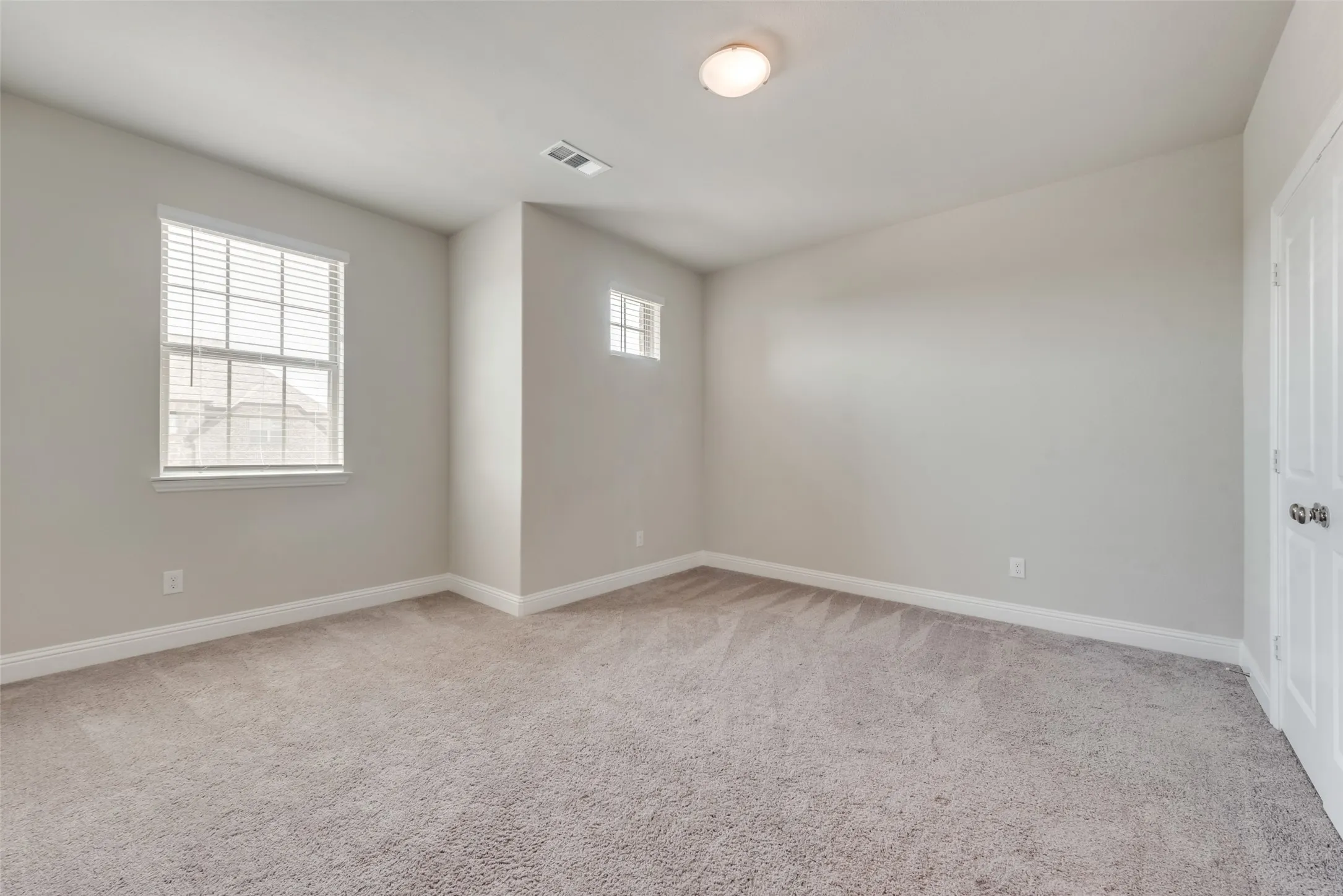 Carpeted interior space featuring neutral wall tones, baseboard molding, a ceiling-mounted light fixture, and two windows with blinds