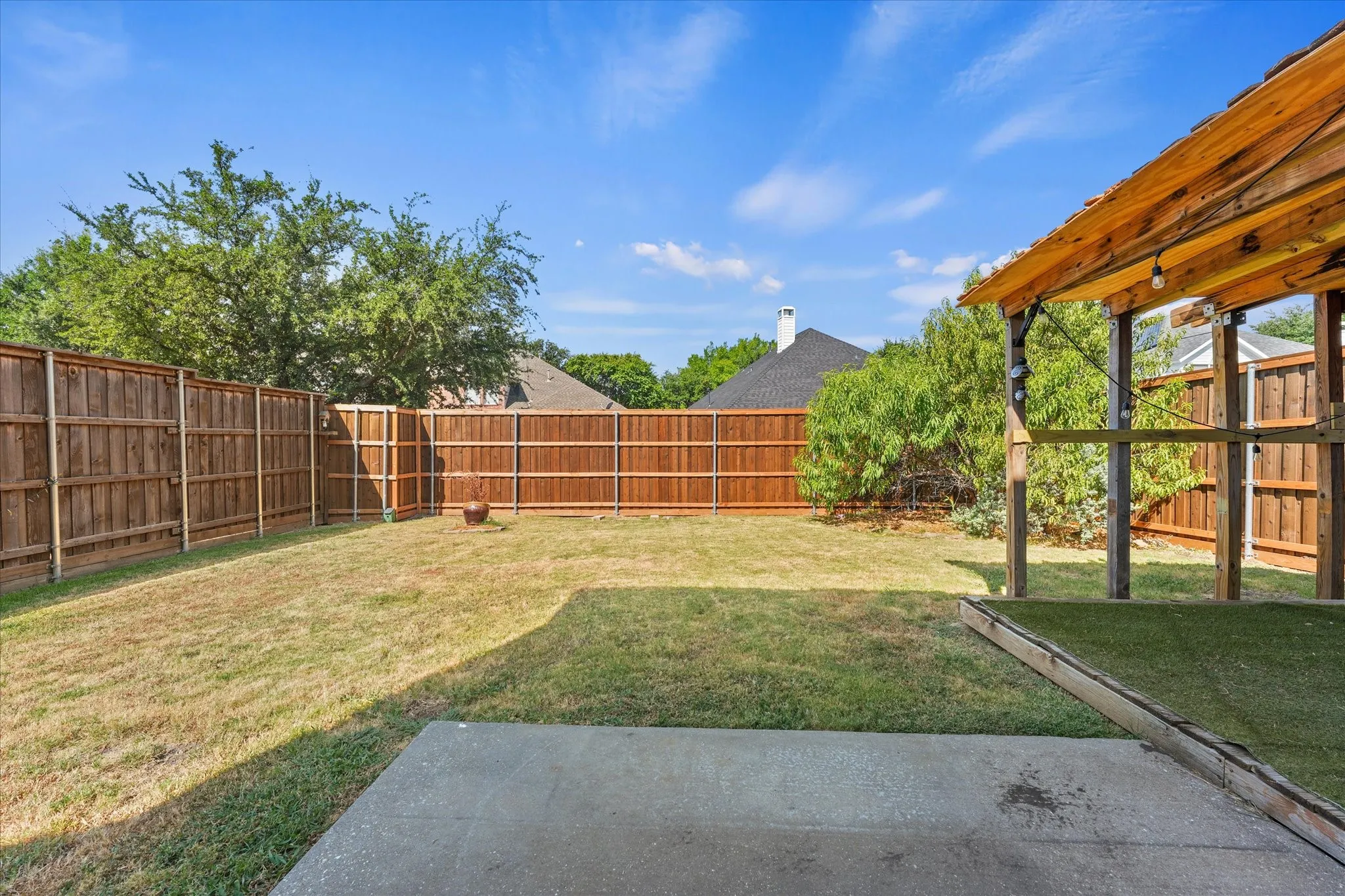 Expansive backyard featuring a concrete patio, wood privacy fencing, and a built-in wood gazebo with string lighting
