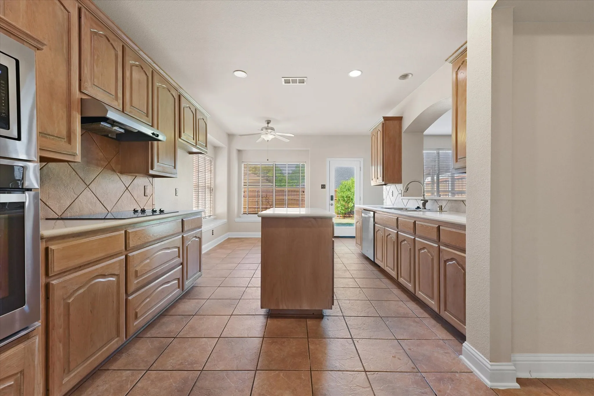 Kitchen featuring a central island with a solid surface countertop, wood cabinetry, tile flooring, and integrated stainless steel appliances