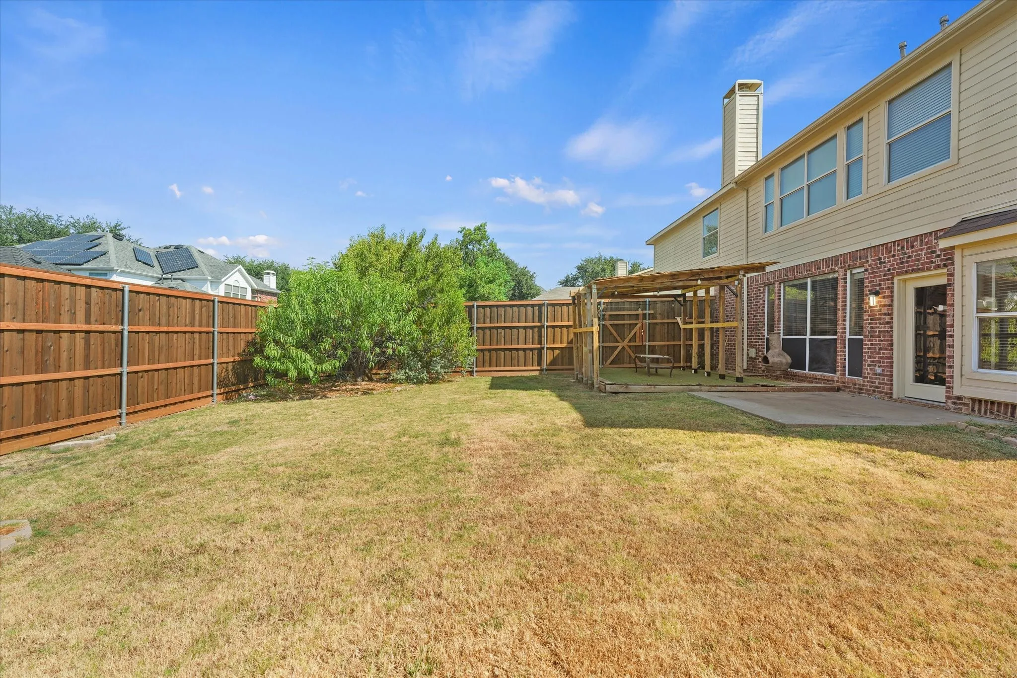 Expansive backyard with a wood privacy fence, concrete patio, and a built-in wooden structure