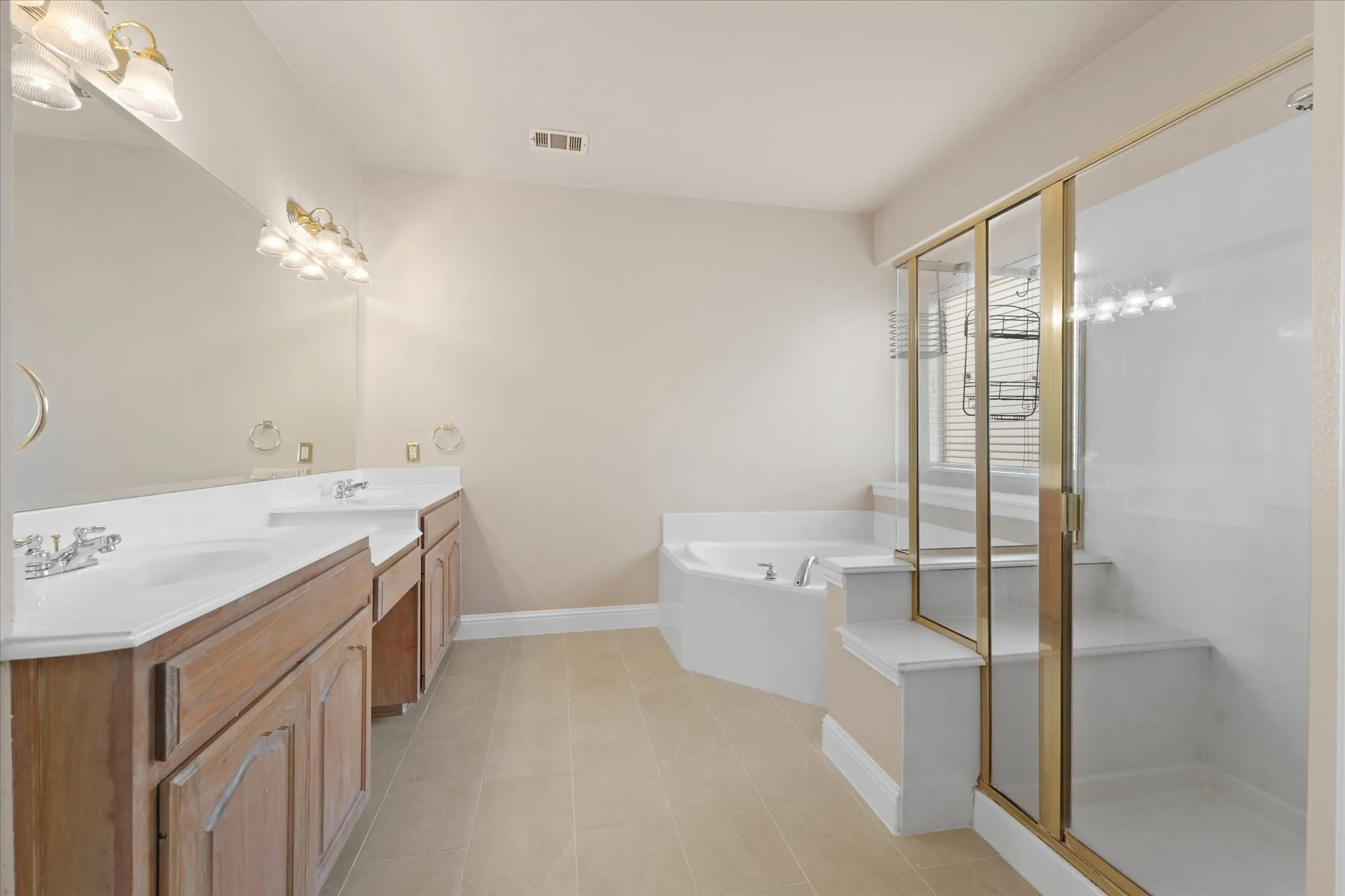 Dual vanity with white countertops, corner soaking tub, walk-in shower with clear glass enclosure, and neutral-toned floor tiling