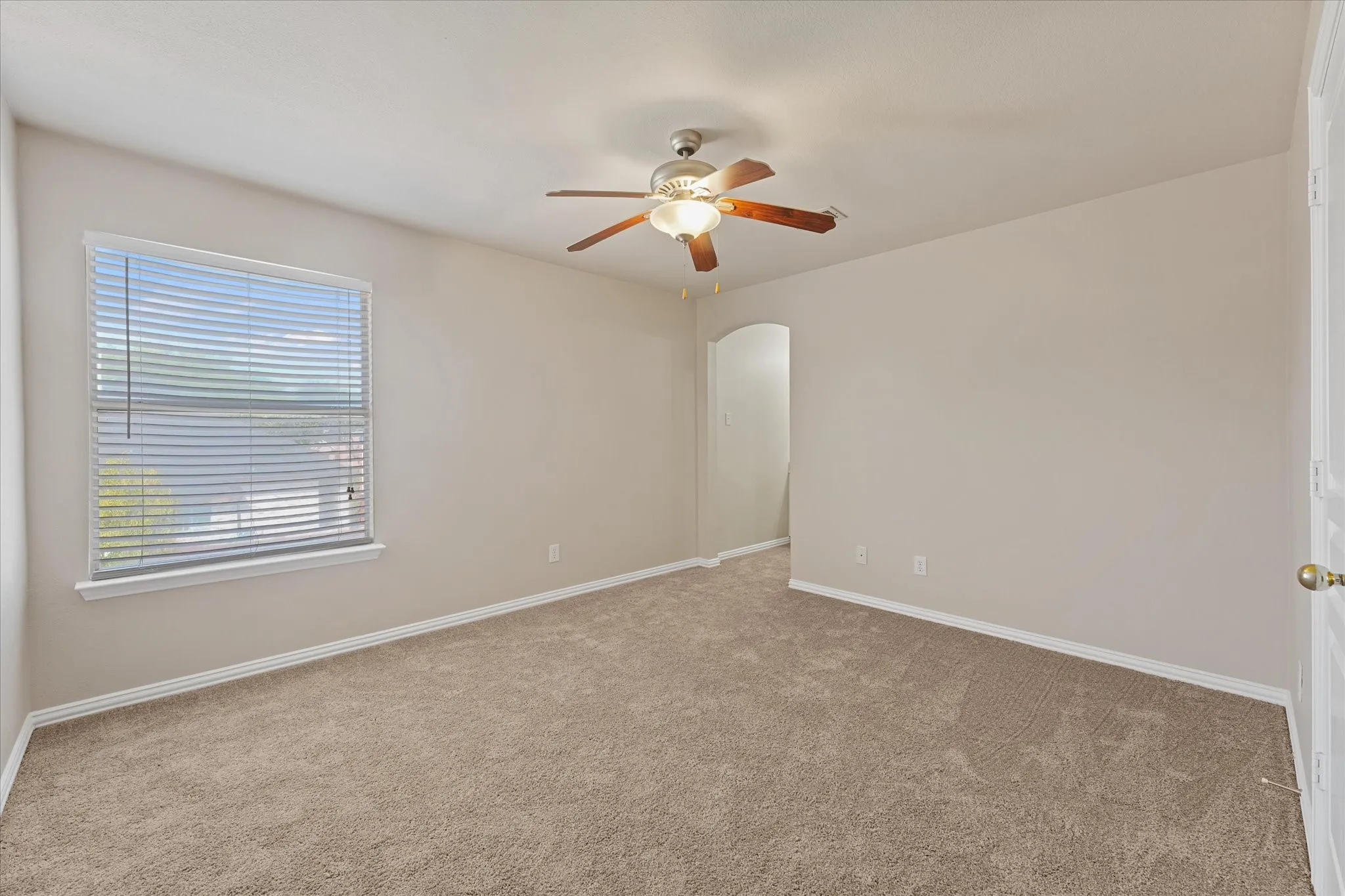 Carpeted room featuring a ceiling fan with light fixture, window with blinds, and an arched doorway