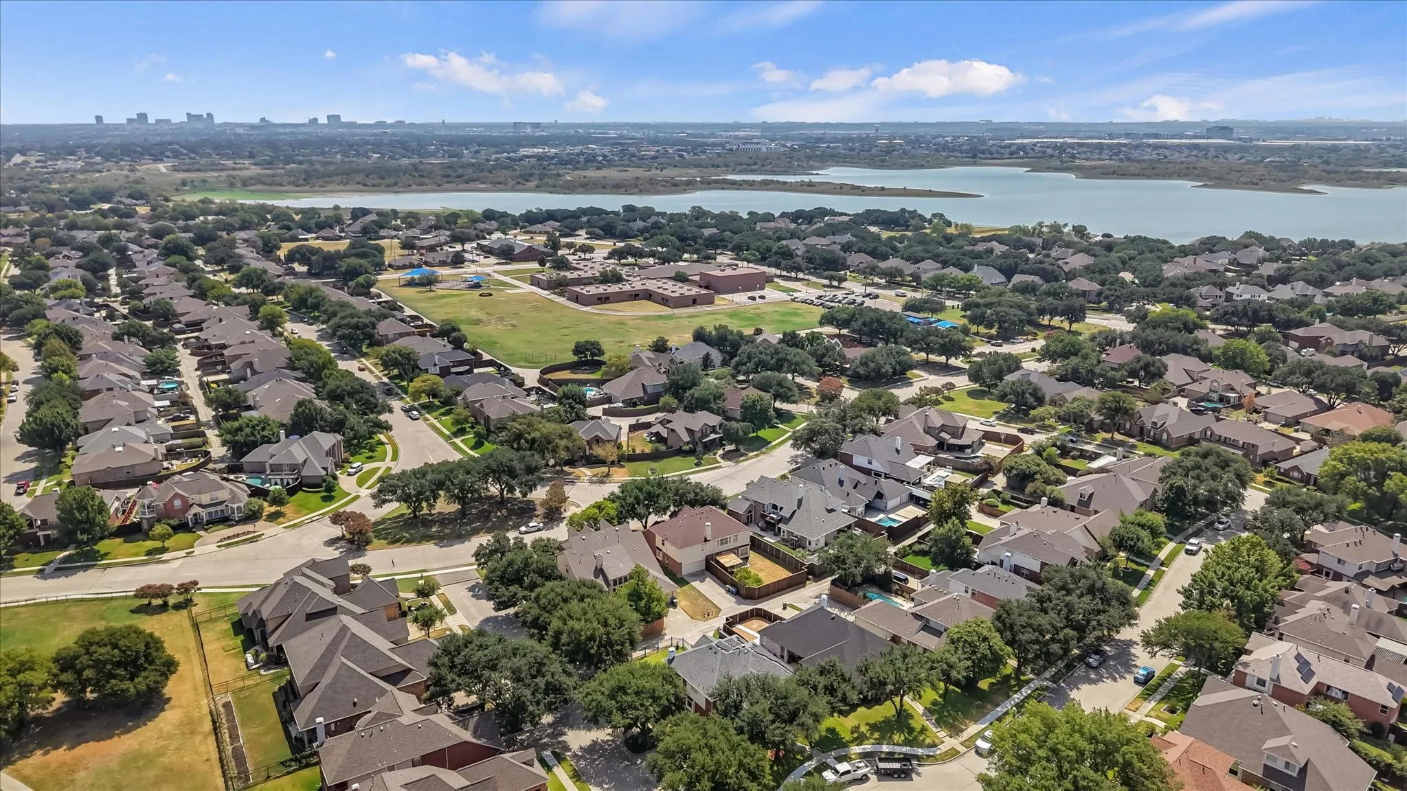 Aerial perspective featuring a residential neighborhood, abundant mature trees, and a distant body of water