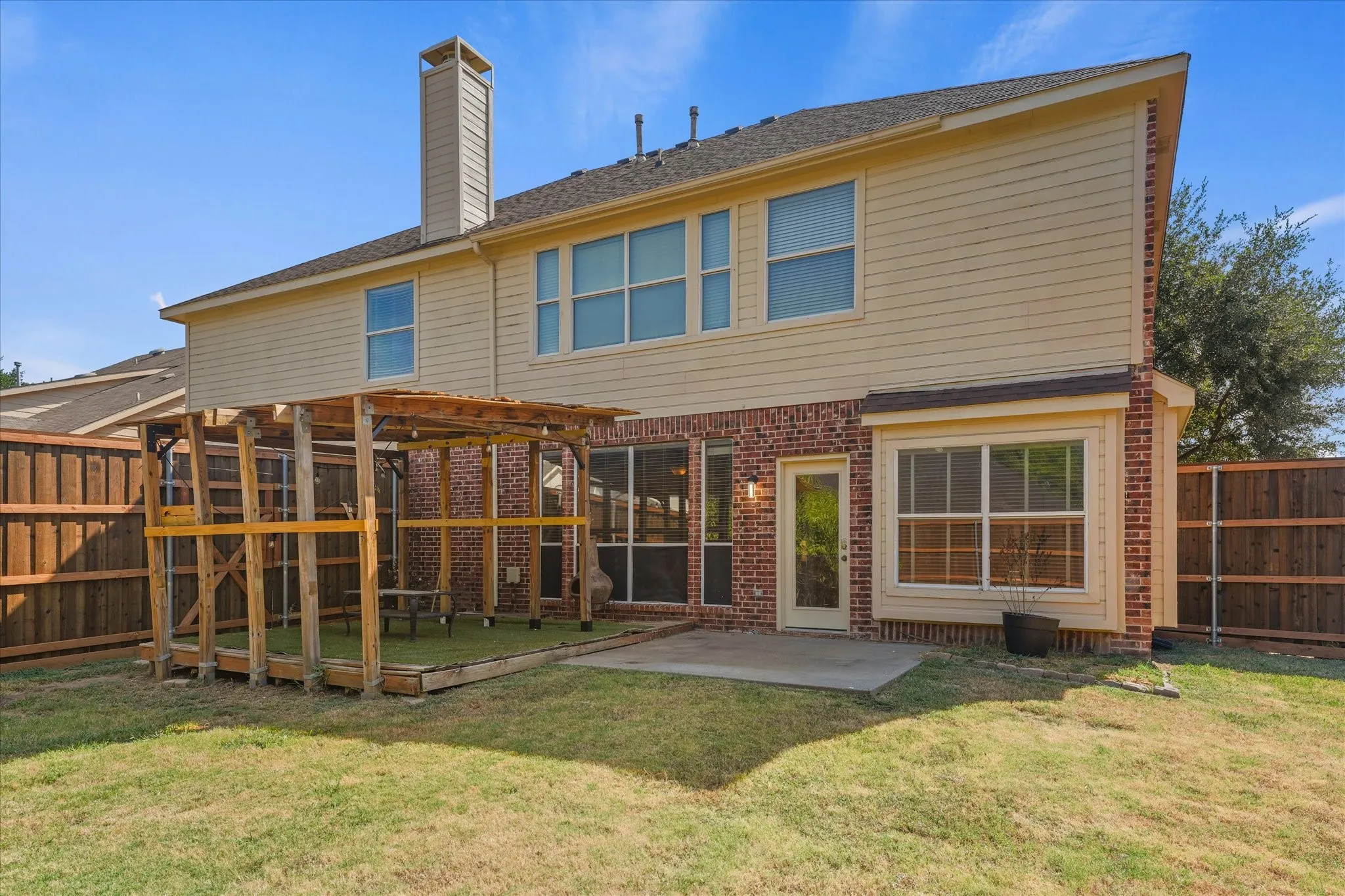 Rear exterior featuring brick and siding facade, private wooden fence, and a built-in wood frame structure