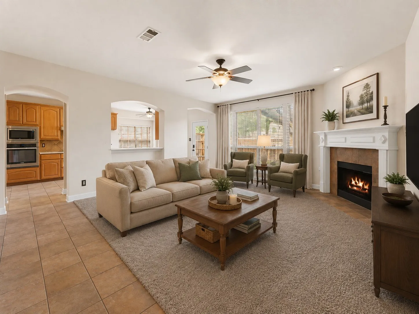 Virtual Staged. Living area featuring a fireplace with a white mantel, ceiling fan with integrated lighting, window with drapes, and carpeted flooring
