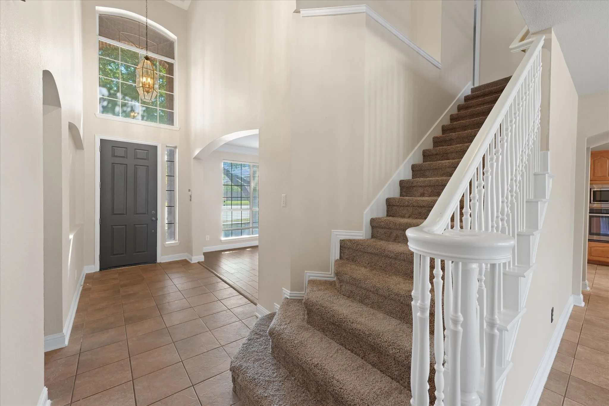 Two-story entry with tile flooring, a paneled entry door, a multi-pane arched window, and a grand staircase with white balusters
