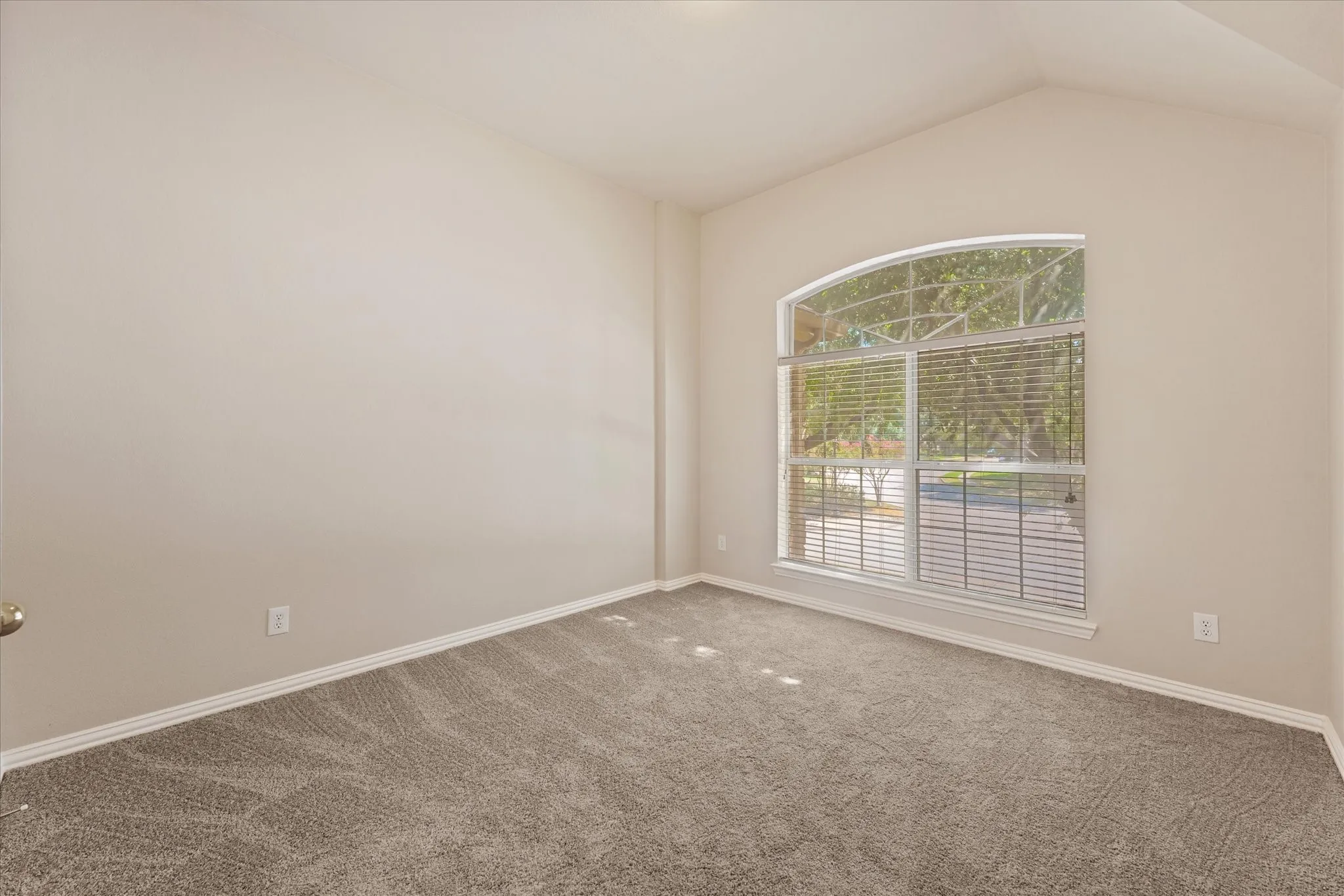 Arched window with blinds, vaulted ceiling, neutral wall color, and carpeted flooring