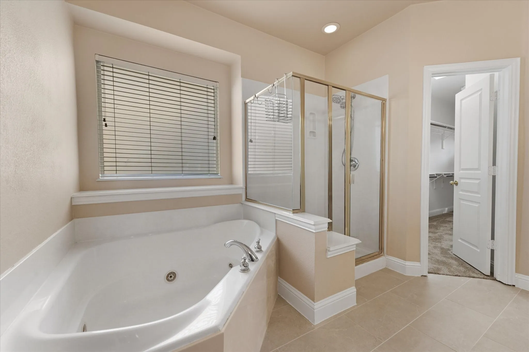 Soaking tub with chrome fixtures, glass-enclosed shower with gold-tone framing, recessed lighting, and tile flooring