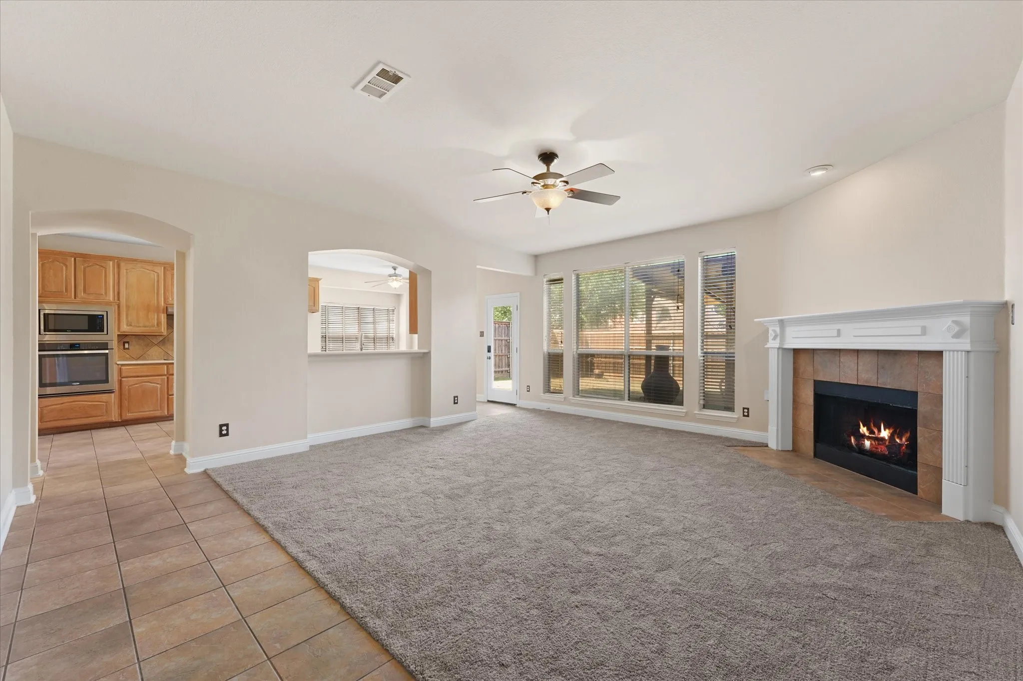 Living area featuring a fireplace with a tile surround, large windows, ceiling fan, and carpet flooring
