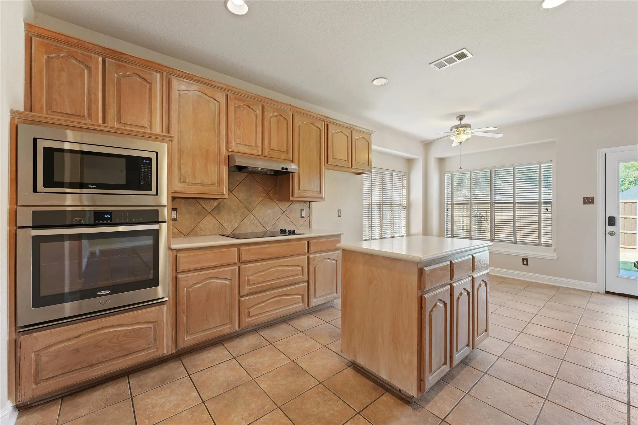 Wood cabinetry with recessed panels, stainless steel built-in appliances, a tiled backsplash, a central island with countertop, and ceramic tile flooring