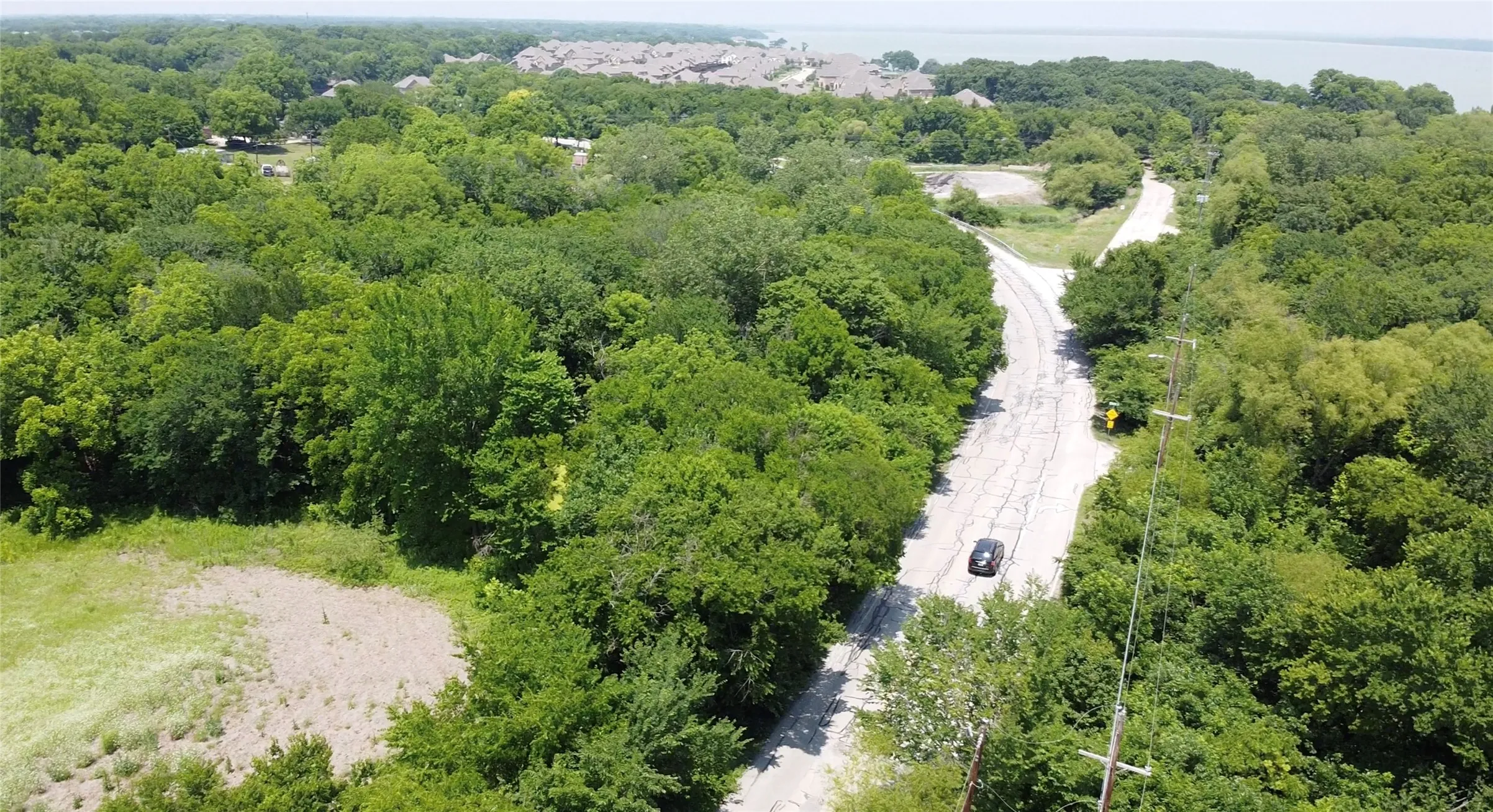 Expansive treed landscape featuring a paved road, a separate unpaved road, and distant water