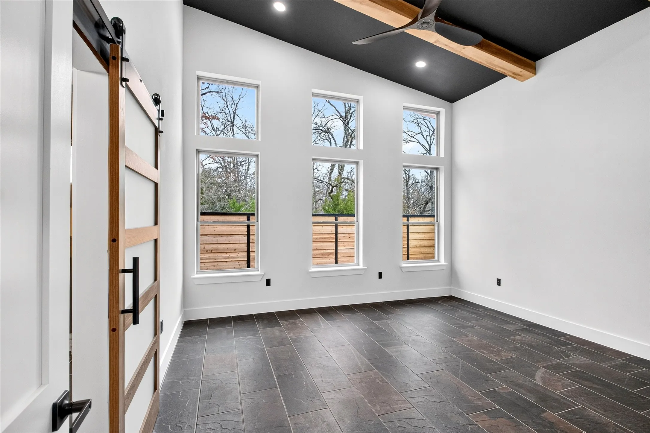Empty room with a barn door, vaulted ceiling, recessed lighting, and ceiling fan