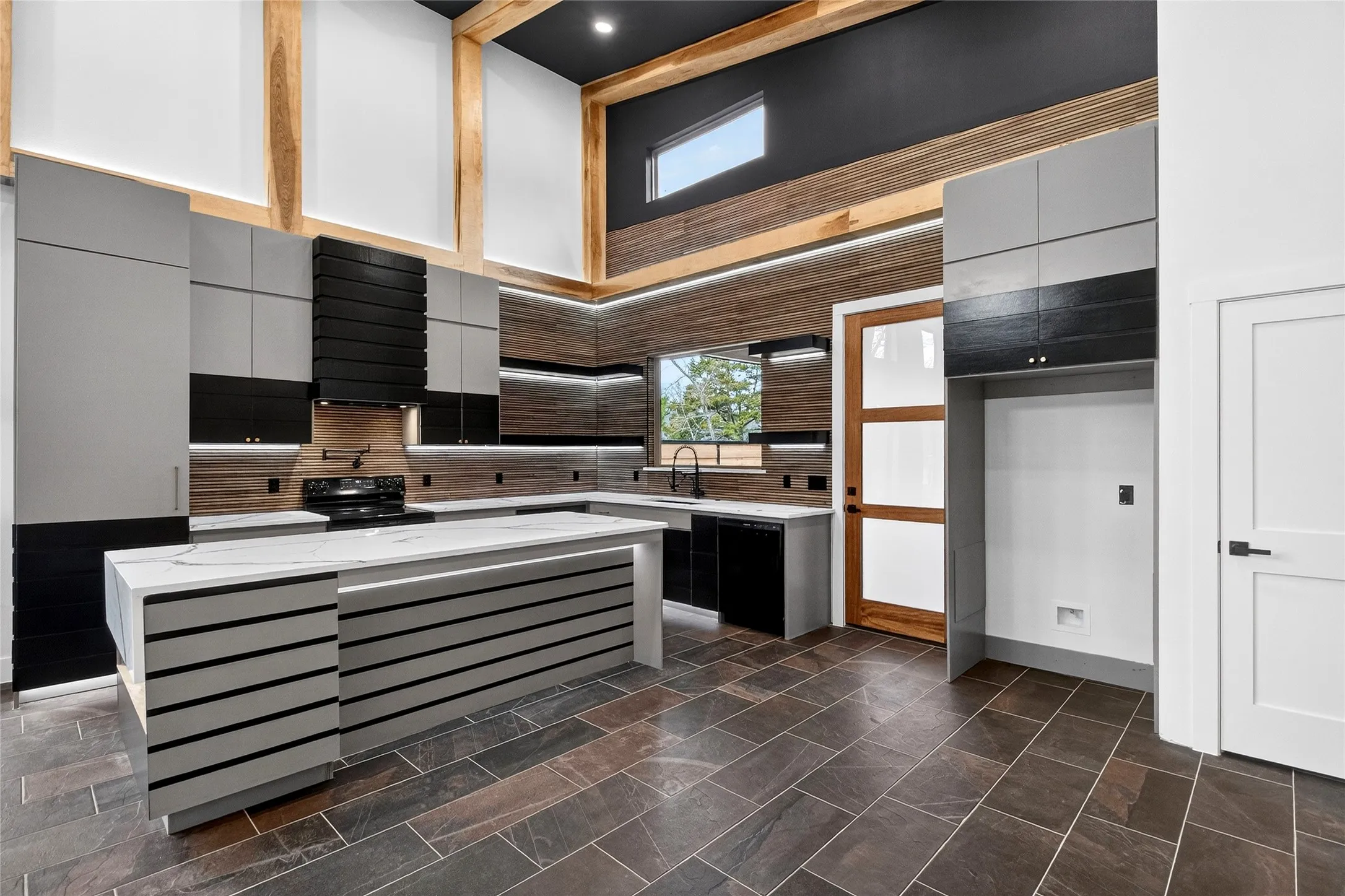Kitchen featuring light stone counters, a high ceiling, a center island, black appliances, and modern cabinets
