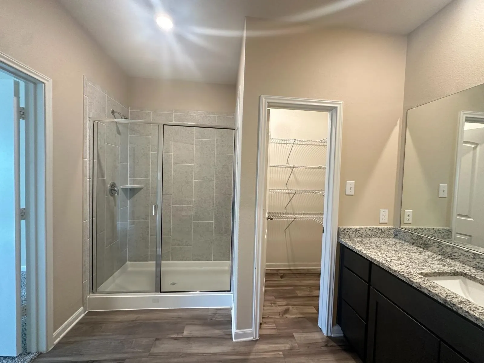 Bathroom featuring a glass-enclosed shower with tile surround, a spacious vanity with a speckled countertop and integrated sink, dark wood-finish cabinetry, and wood-finish flooring