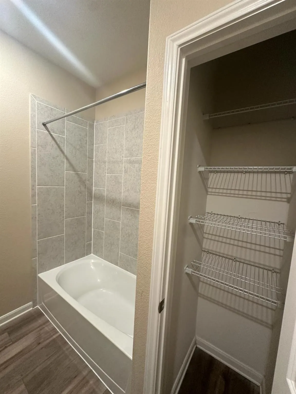 Bathroom featuring a white bathtub with light gray rectangular tile surround and a chrome shower rod