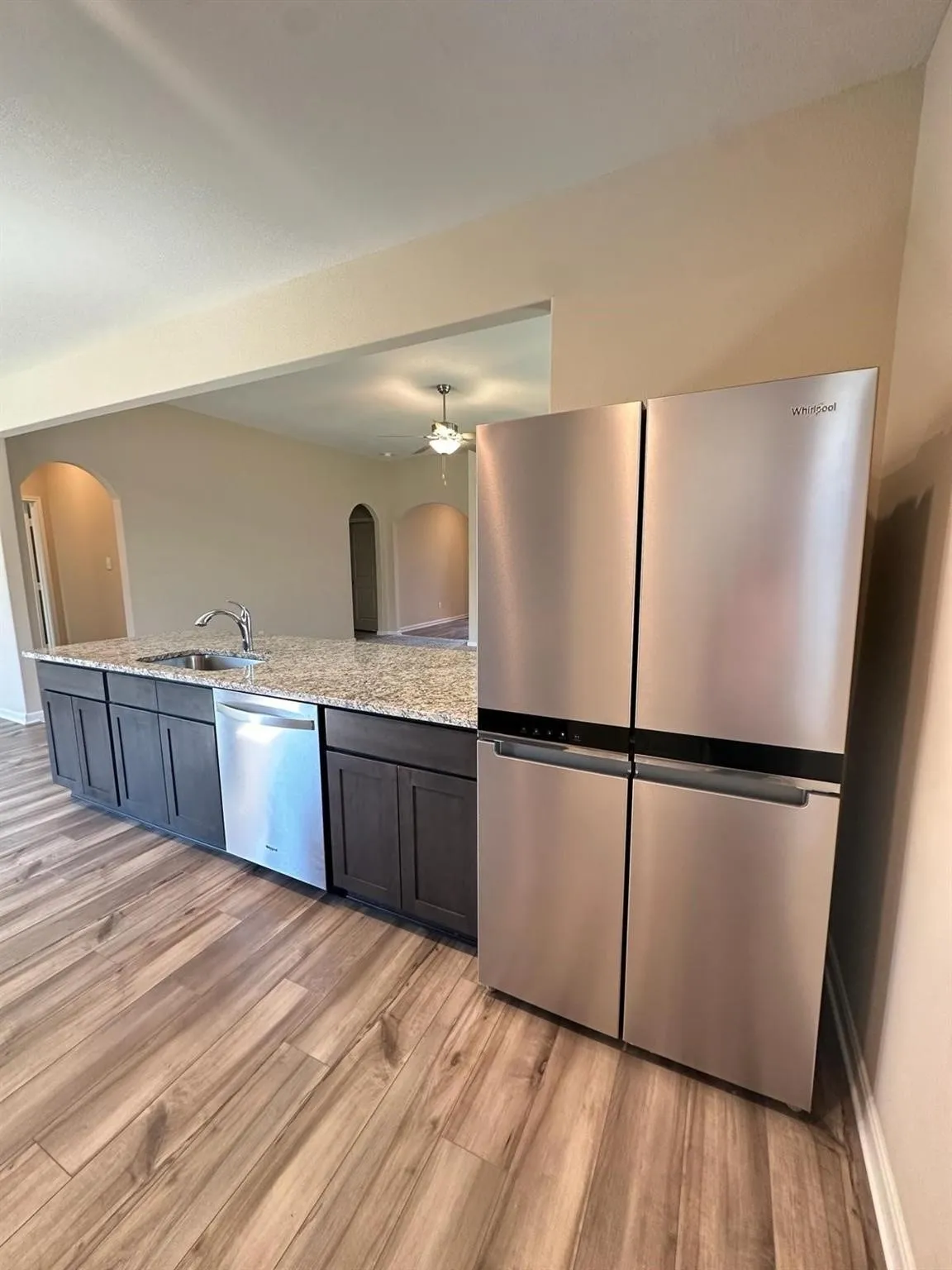 Stainless steel refrigerator and dishwasher with a large island featuring dark cabinetry and a speckled countertop