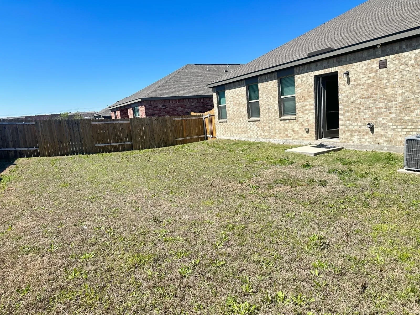 Expansive backyard featuring a privacy fence, brick exterior, multiple windows, and a patio door