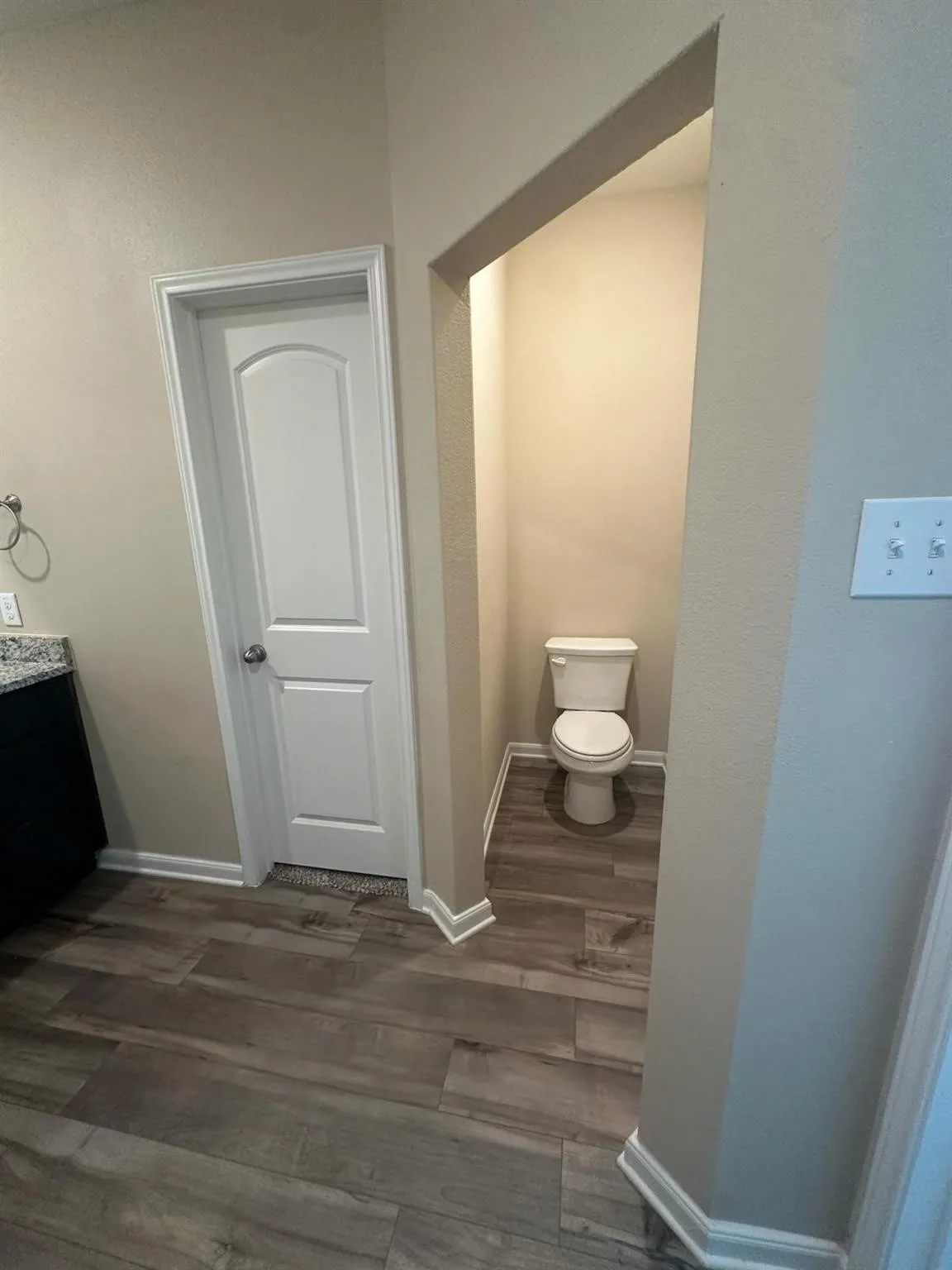 Dedicated water closet featuring wood-finish flooring, neutral wall tones, and crisp white baseboards