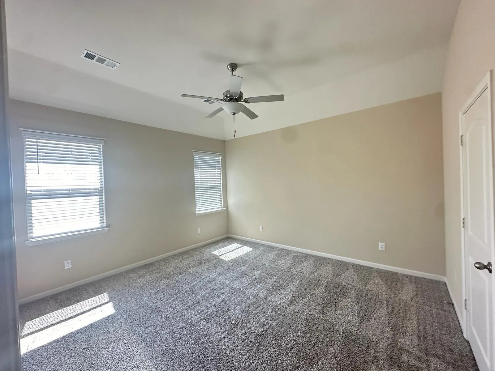 Spacious room featuring vaulted ceilings, two windows with blinds, neutral-toned walls, and patterned carpeting