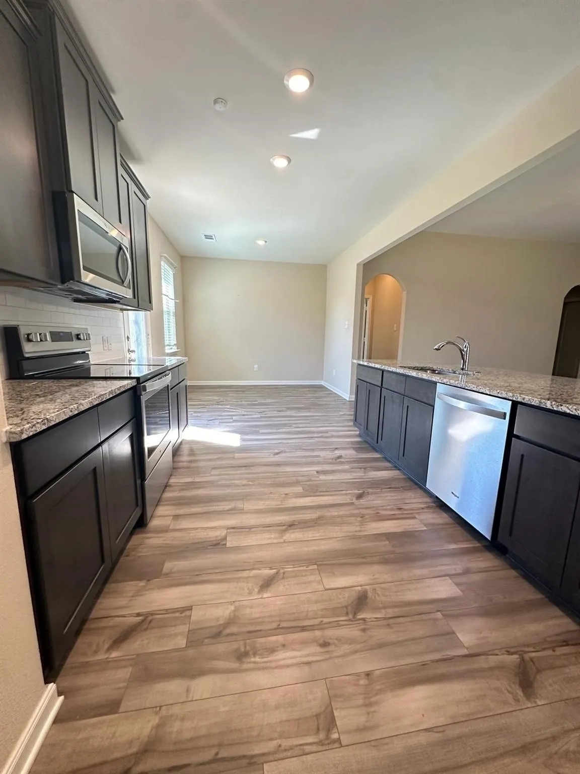 Modern kitchen featuring dark cabinetry, stainless steel appliances, speckled stone countertops, and wood-finish flooring