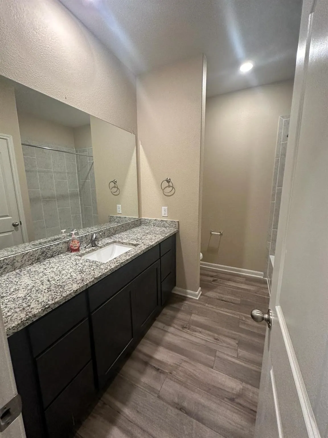 Spacious bathroom featuring a long vanity with a light granite countertop, dark cabinetry, and a large mirror