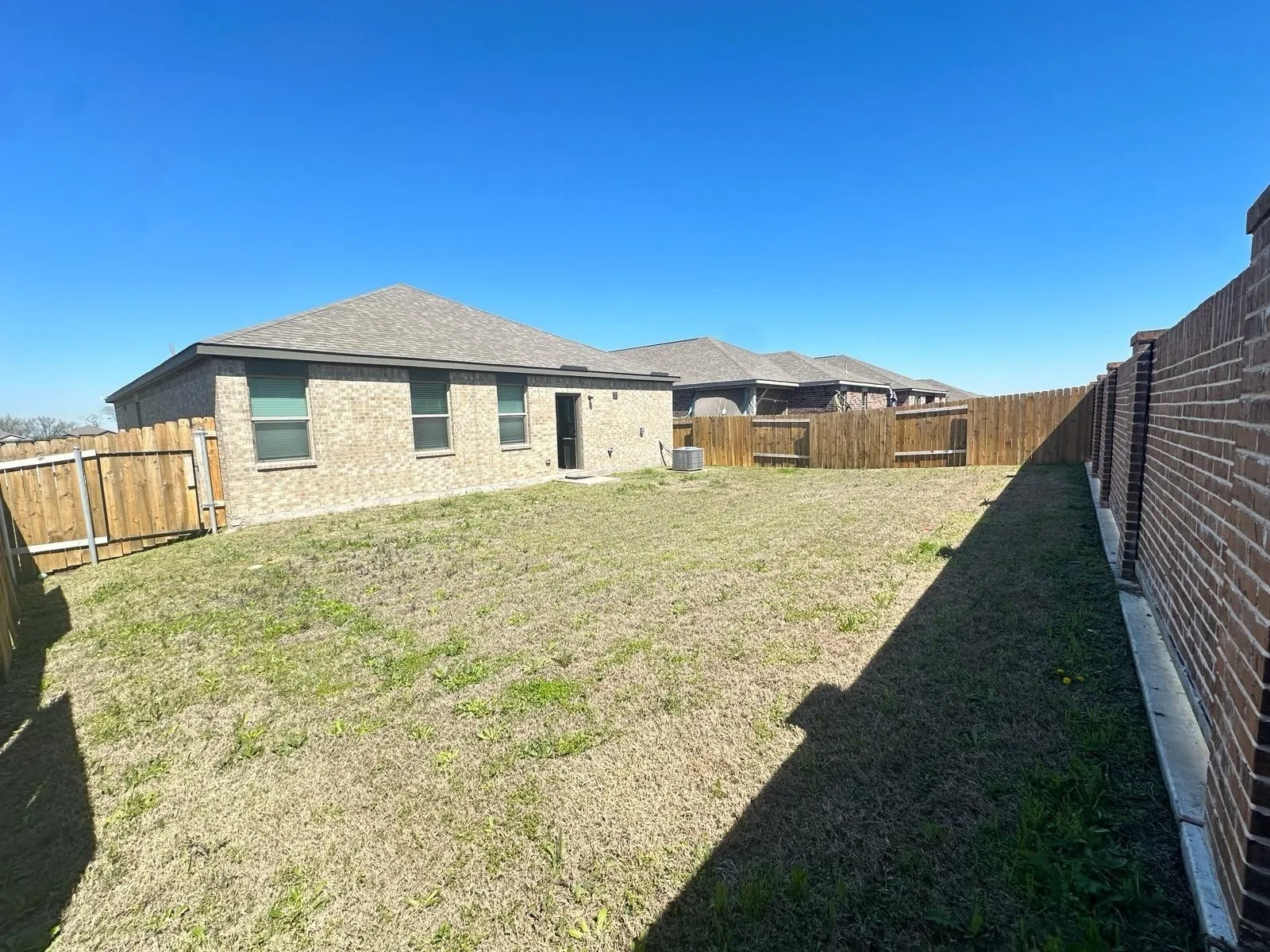 Fenced backyard featuring a mix of wood privacy fencing and a brick privacy wall