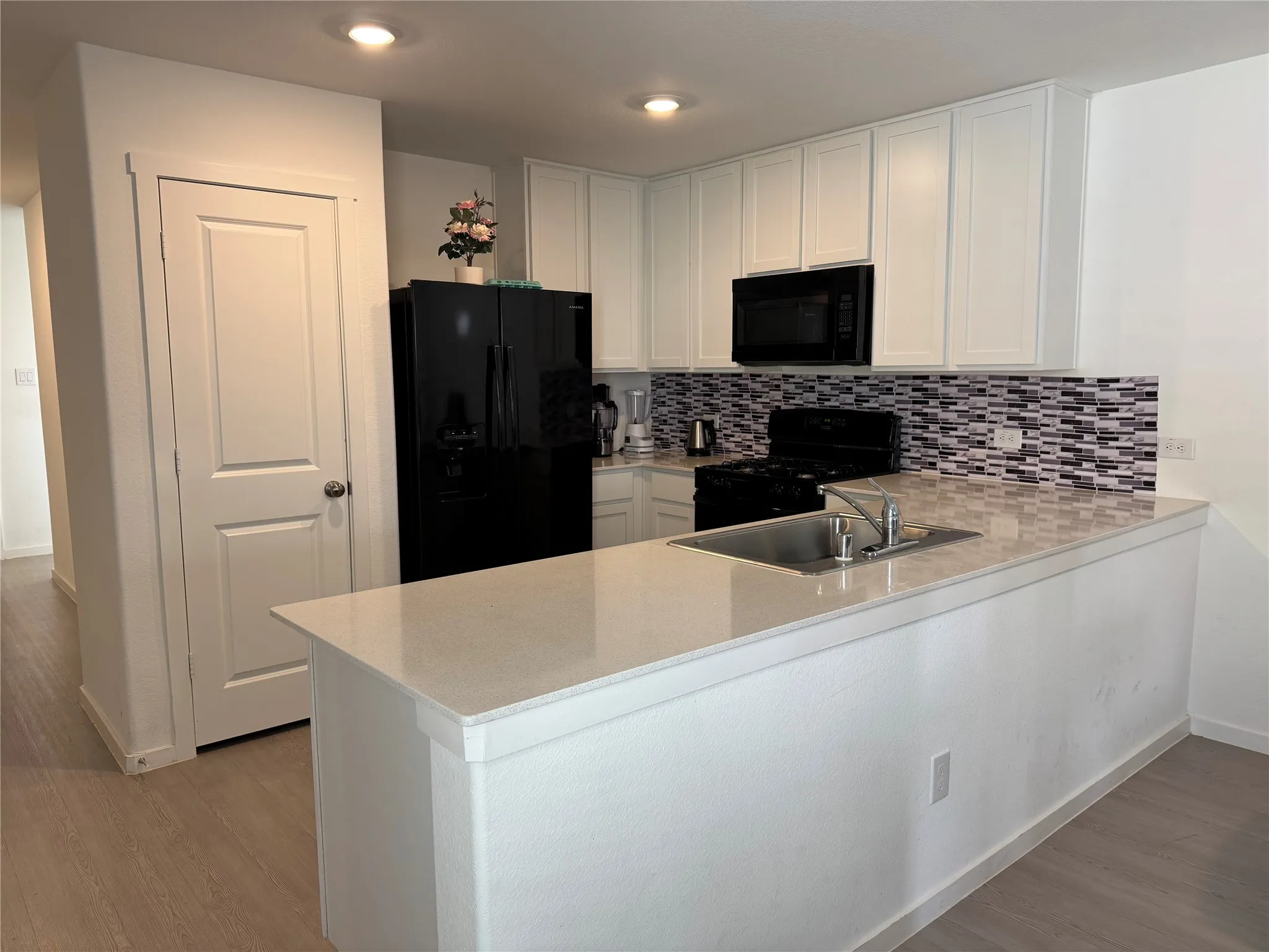 Kitchen featuring white cabinetry, a mosaic tile backsplash, black appliances, a stainless steel sink, and light wood-finish flooring