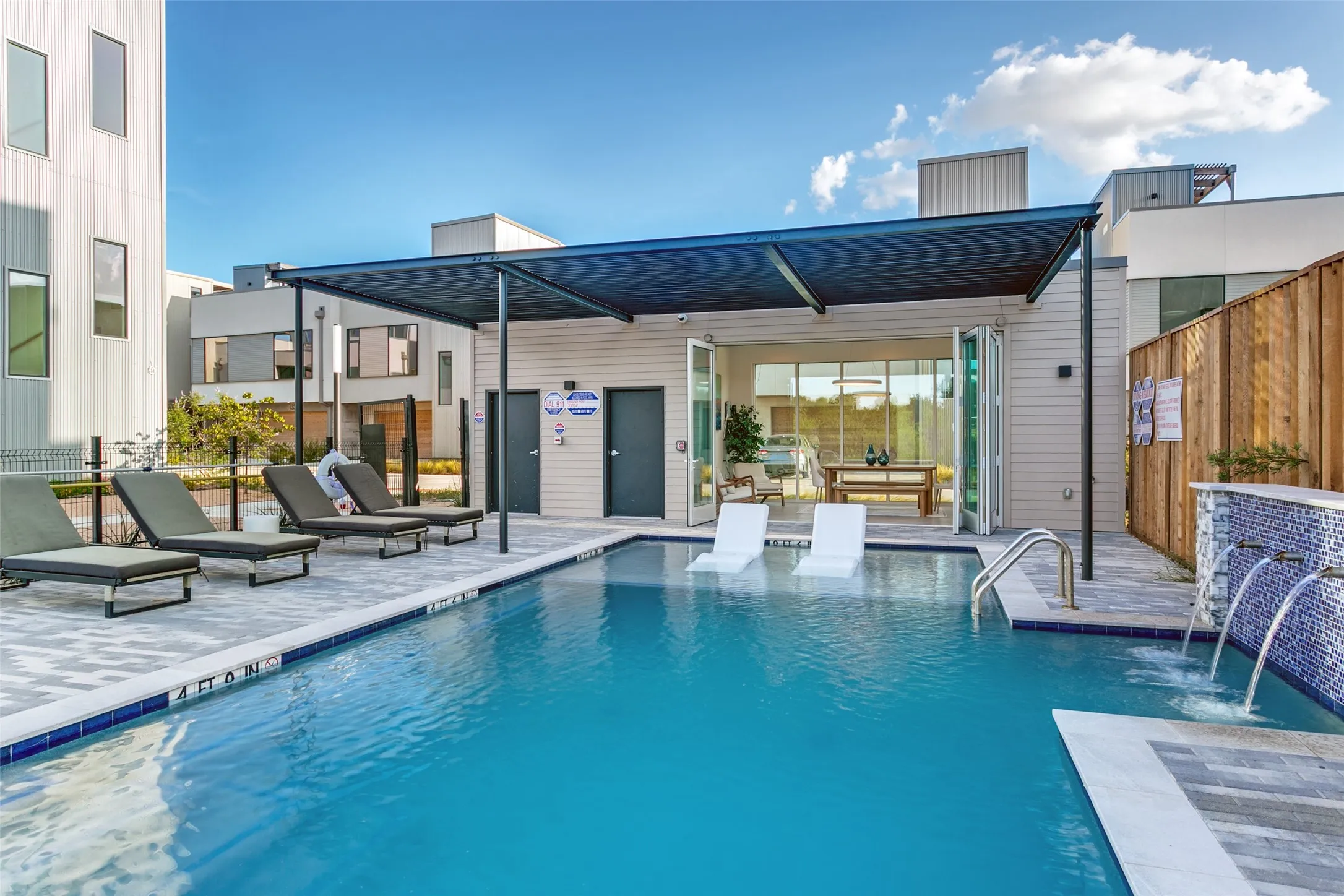 Swimming pool with integrated sun ledges, decorative tiled water features, paved surround, and covered outdoor lounge area