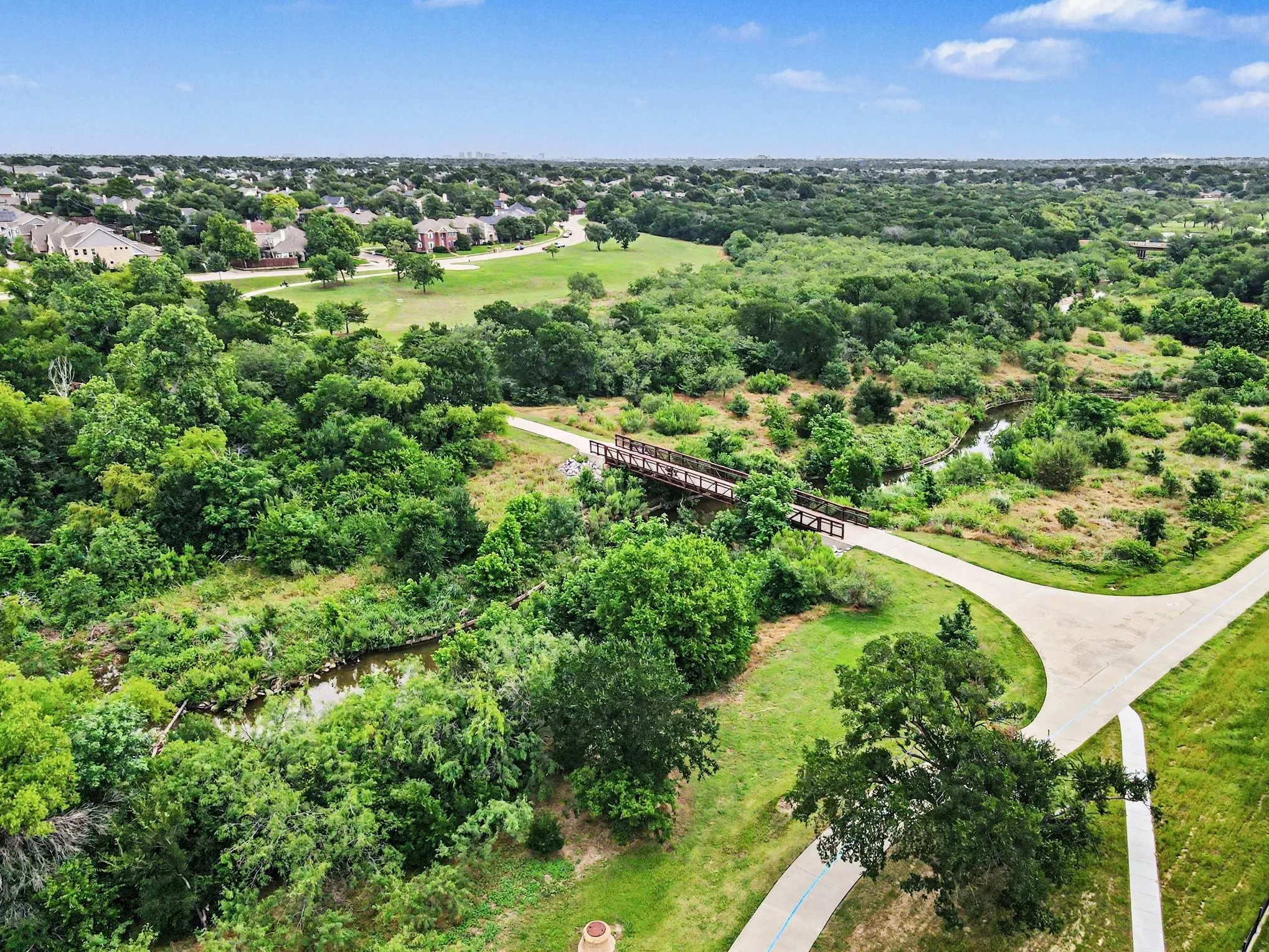 Extensive green space featuring a walking path, mature trees, natural creek, and a pedestrian bridge