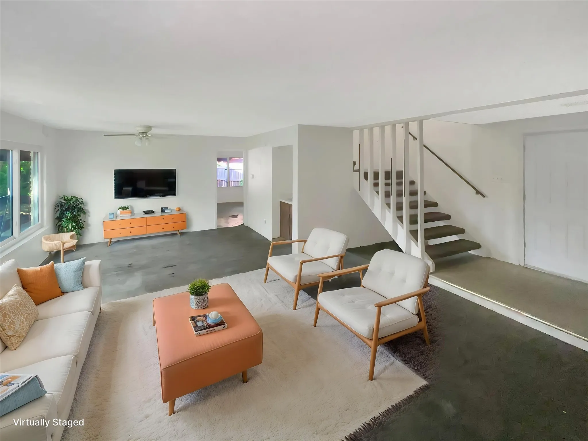 Spacious living area featuring large windows, a ceiling fan, and staircase with railing