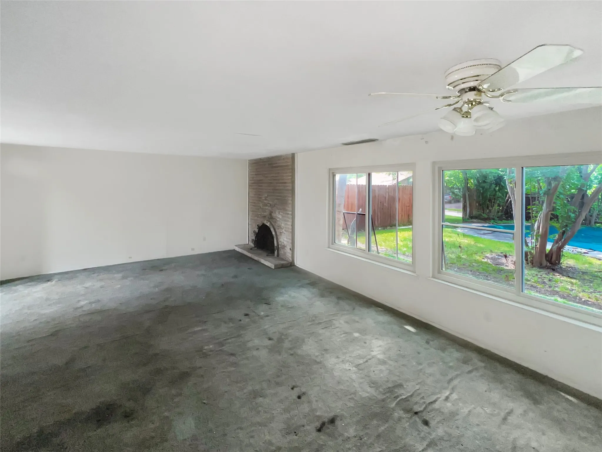 Spacious room featuring a brick fireplace, multiple windows, and a ceiling fan