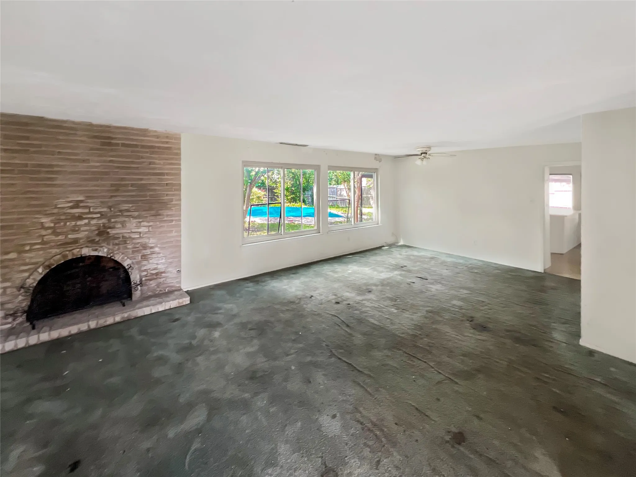 Spacious interior featuring a brick fireplace with a hearth, multiple windows, a ceiling fan, and a glimpse of an outdoor pool