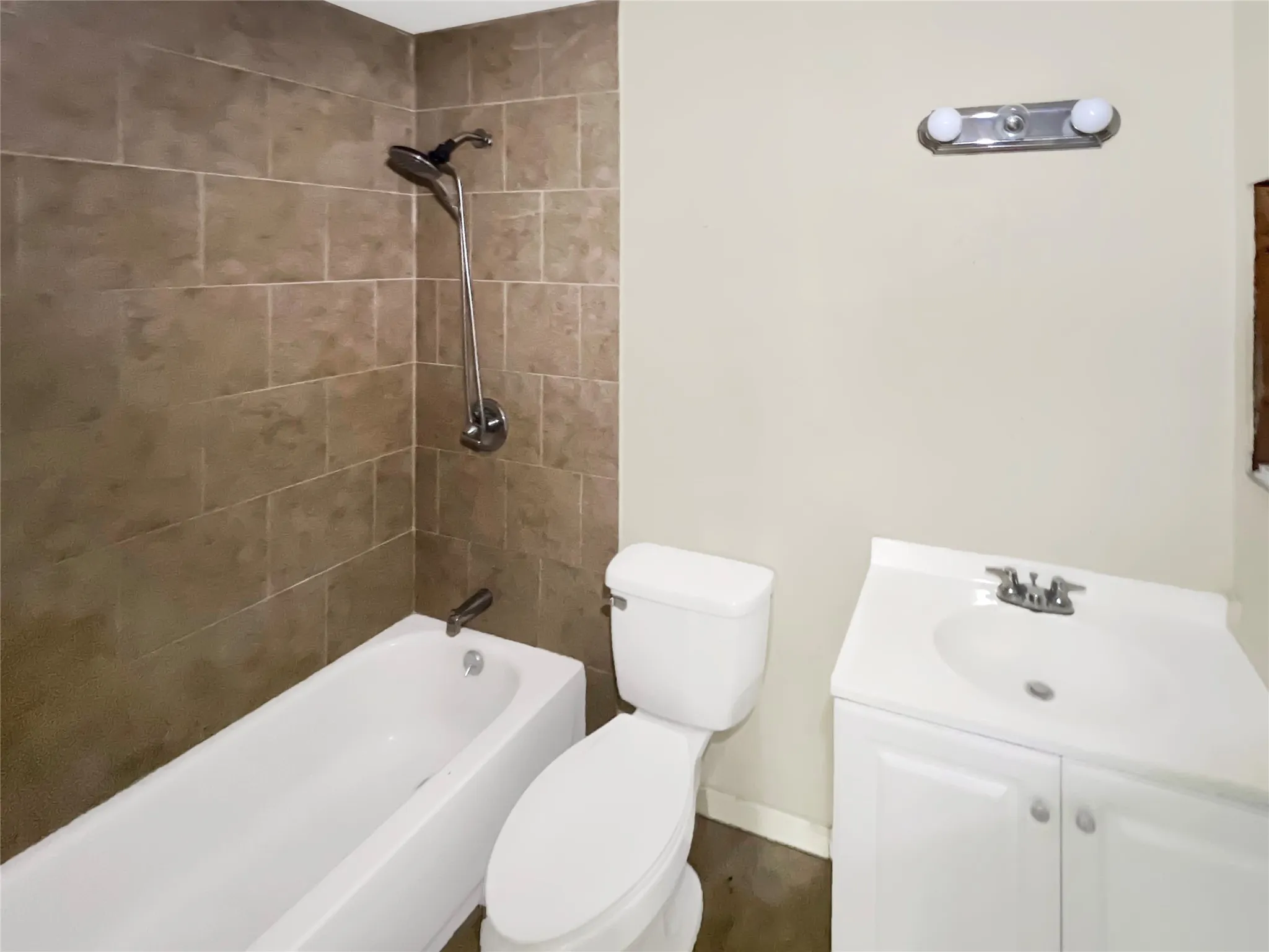 Bathroom featuring a white bathtub, ceramic tile shower surround, chrome shower fixture, white toilet, and a white vanity with an integrated sink and chrome faucet
