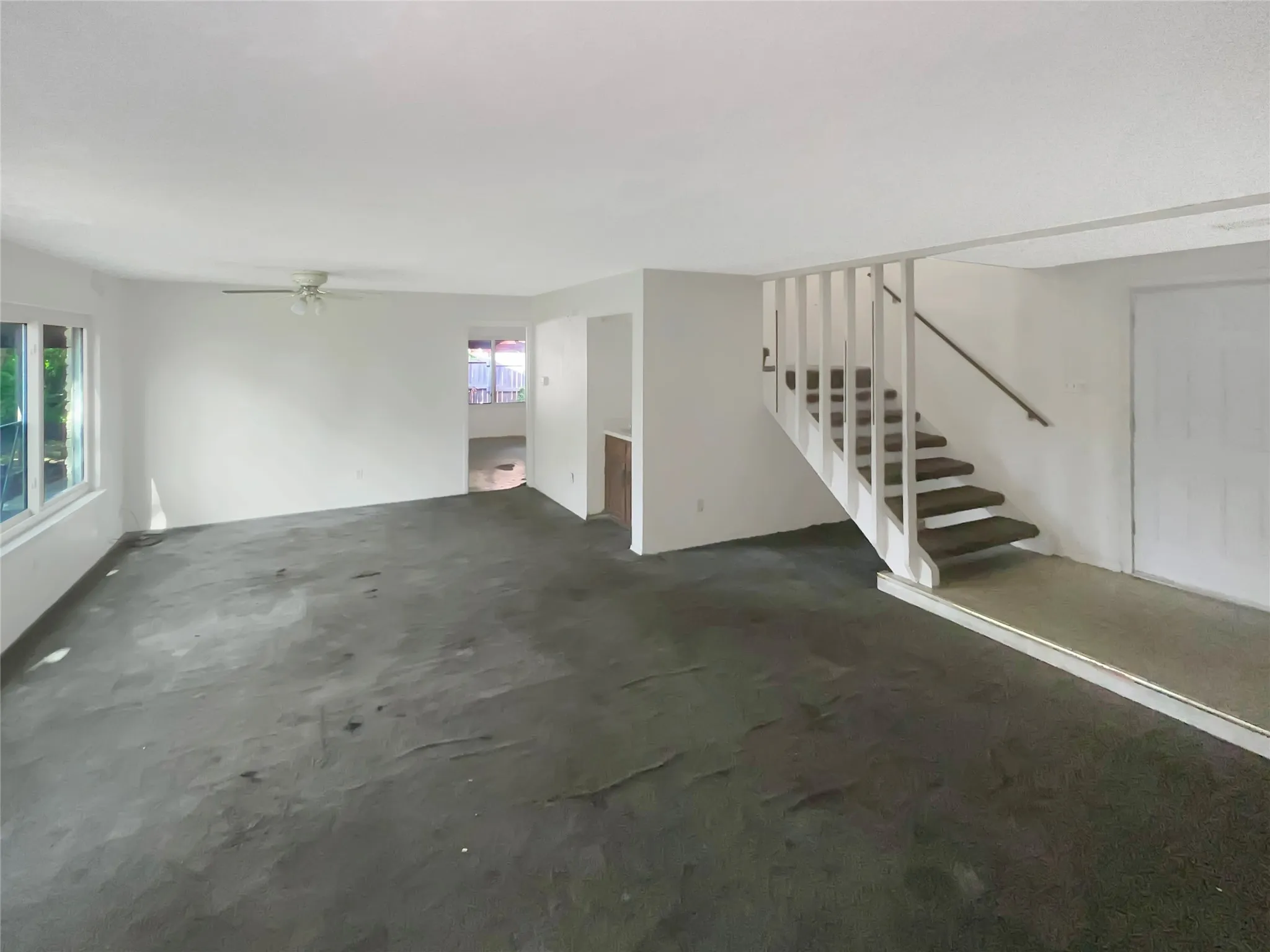 Spacious room featuring multiple windows, a ceiling fan, and a staircase with a white railing