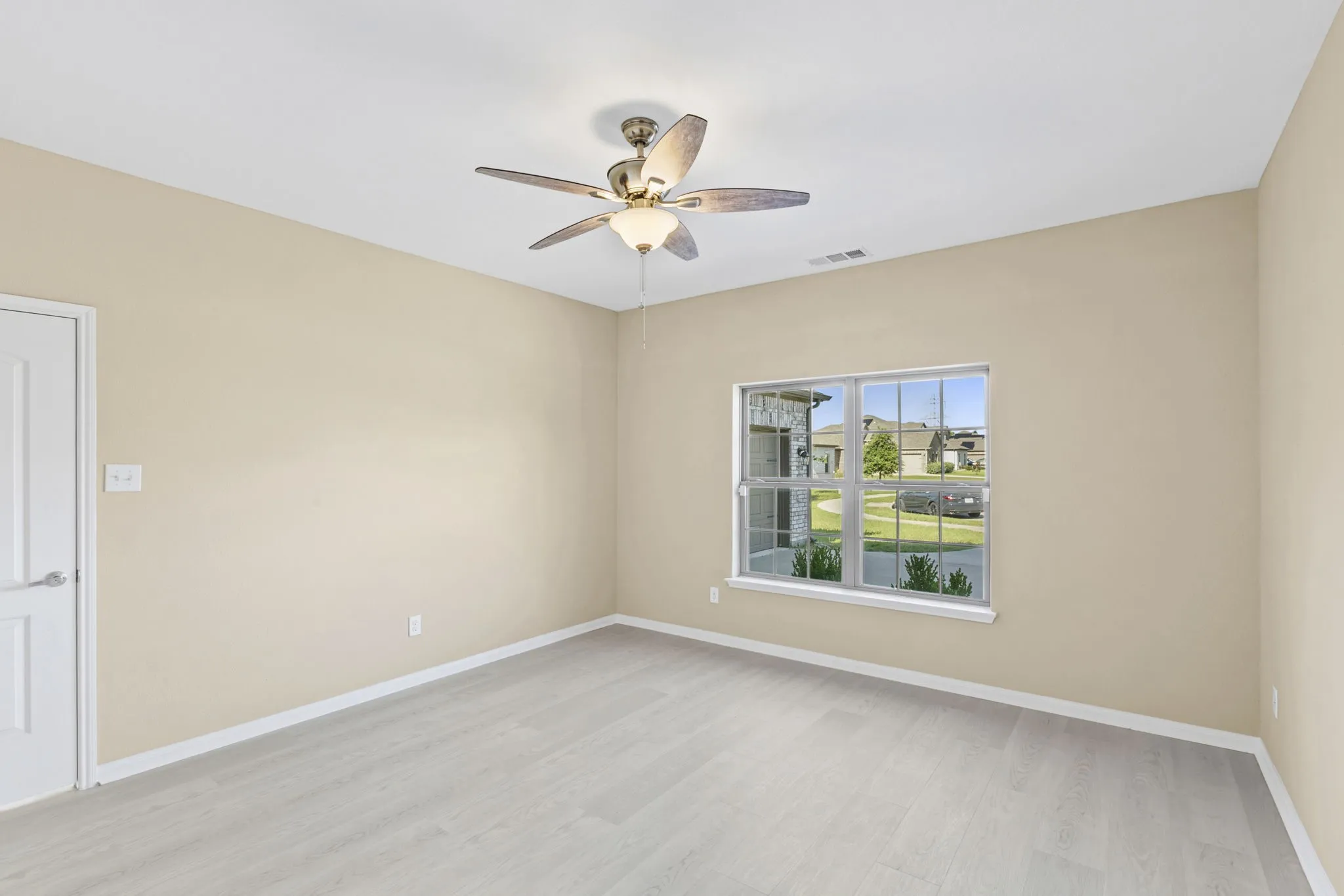 Spacious room featuring light wood-finish flooring, a ceiling fan with integrated lighting, and a white interior door