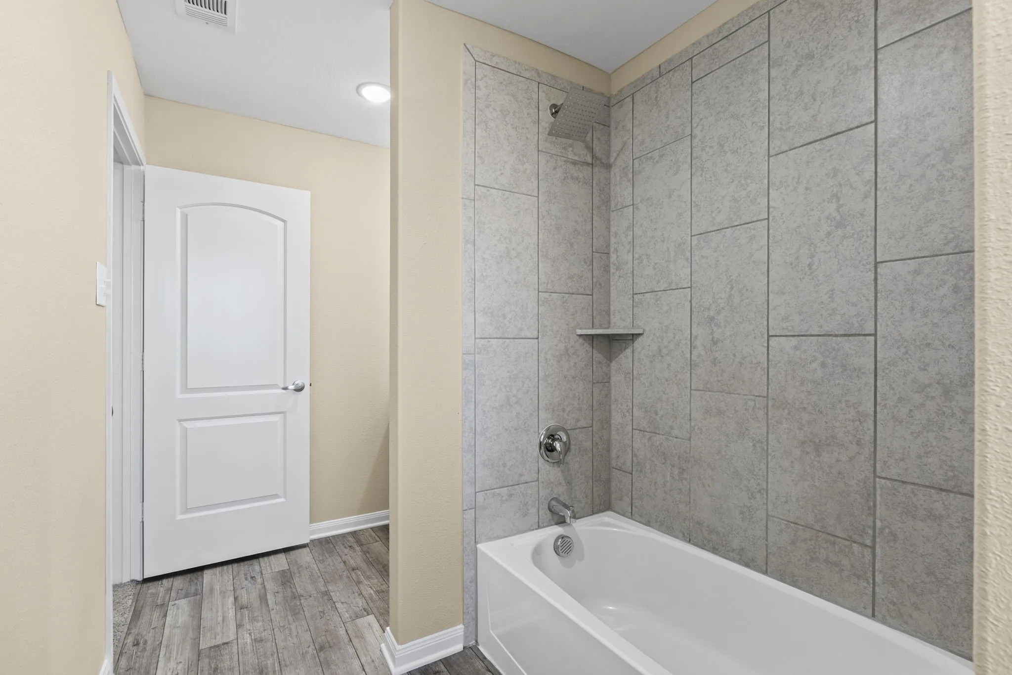 Bathroom featuring a white bathtub, chrome fixtures, and grey large-format tile surround