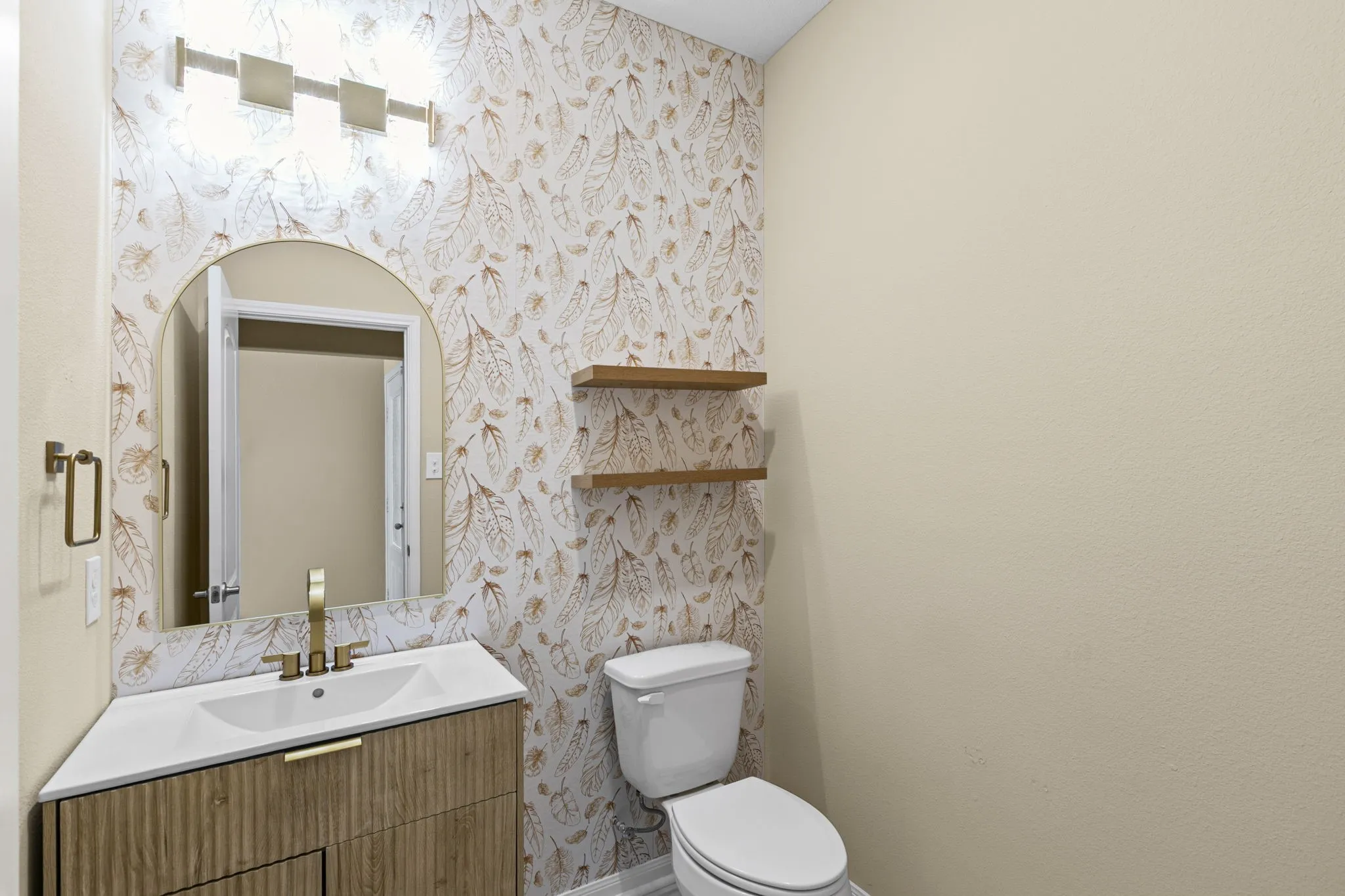 Bathroom vanity featuring a white countertop with integrated sink, gold-finish faucet, and a mirror with an arched top